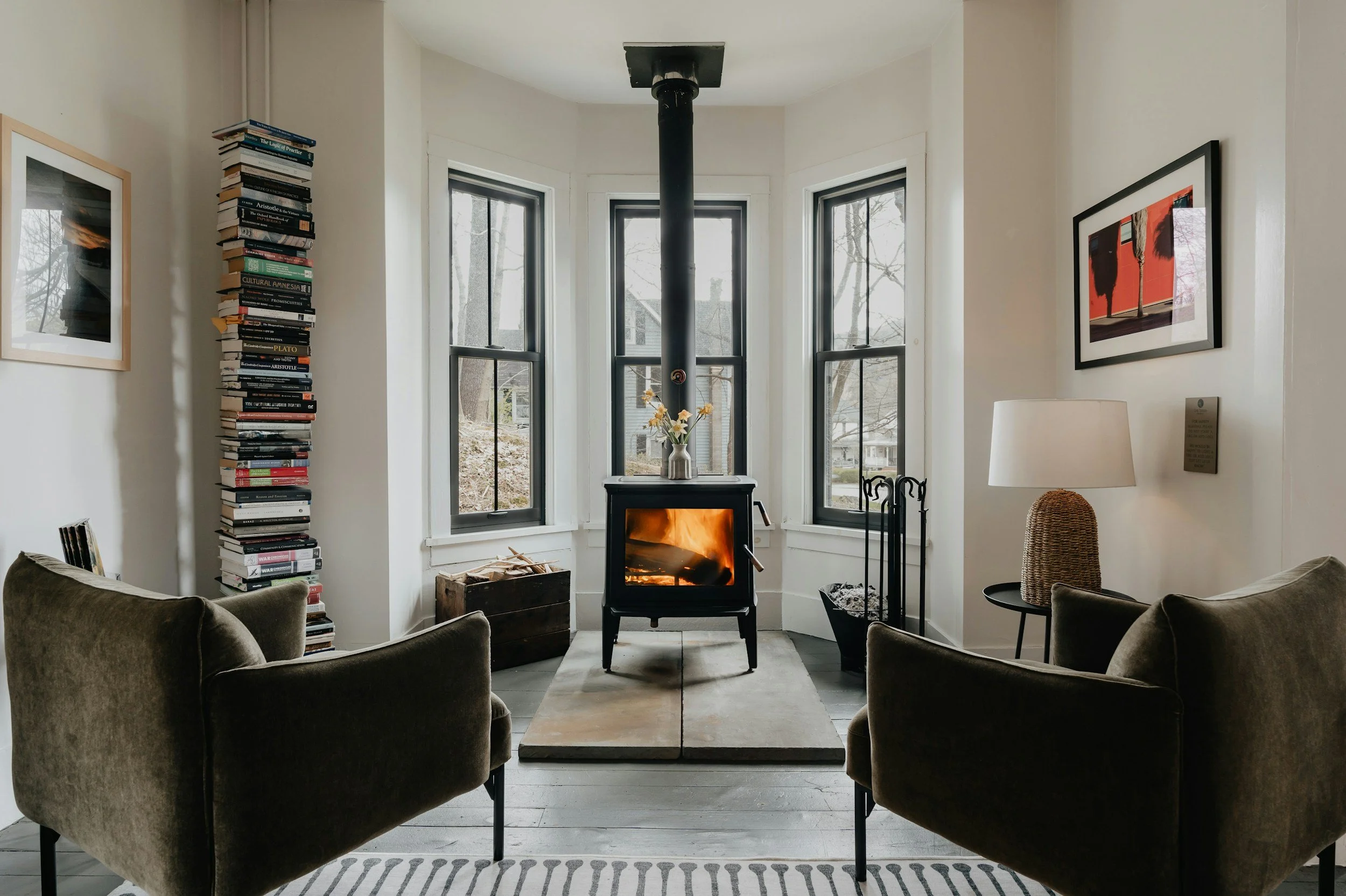 Living room with a wood stove, two armchairs, a bookshelf, and artwork.