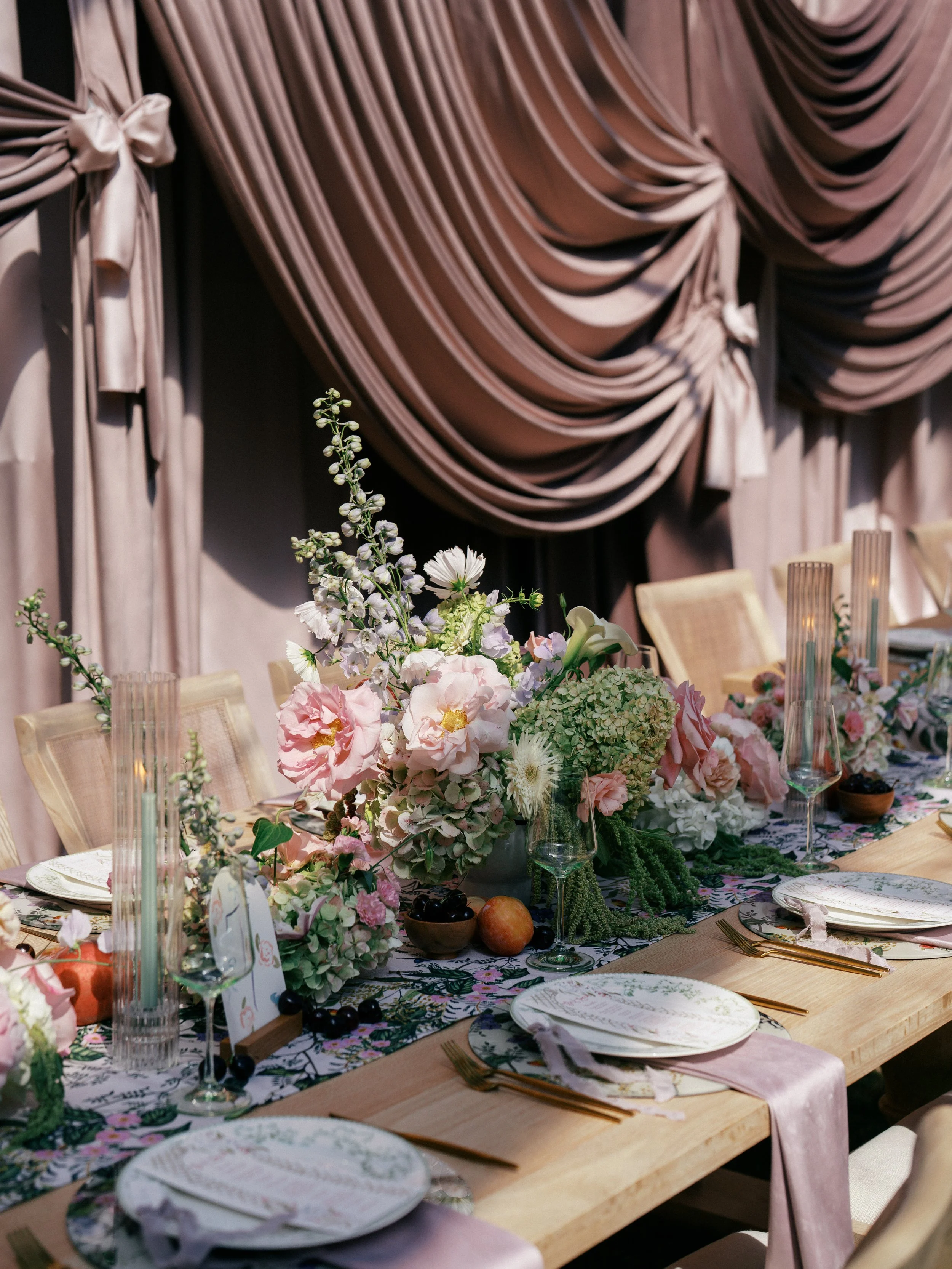 Elegant dining table with floral centerpiece, pink and white flowers, and pink drapes in the background.