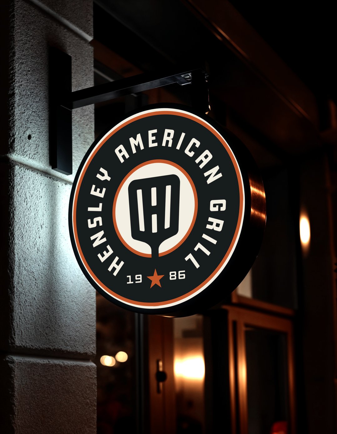 Round hanging sign for Hensley American Grill featuring a vintage badge logo and spatula icon.