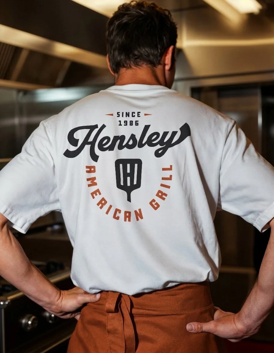 Hensley American Grill staff uniform shirt with vintage script logo, spatula icon, and American grill lettering.