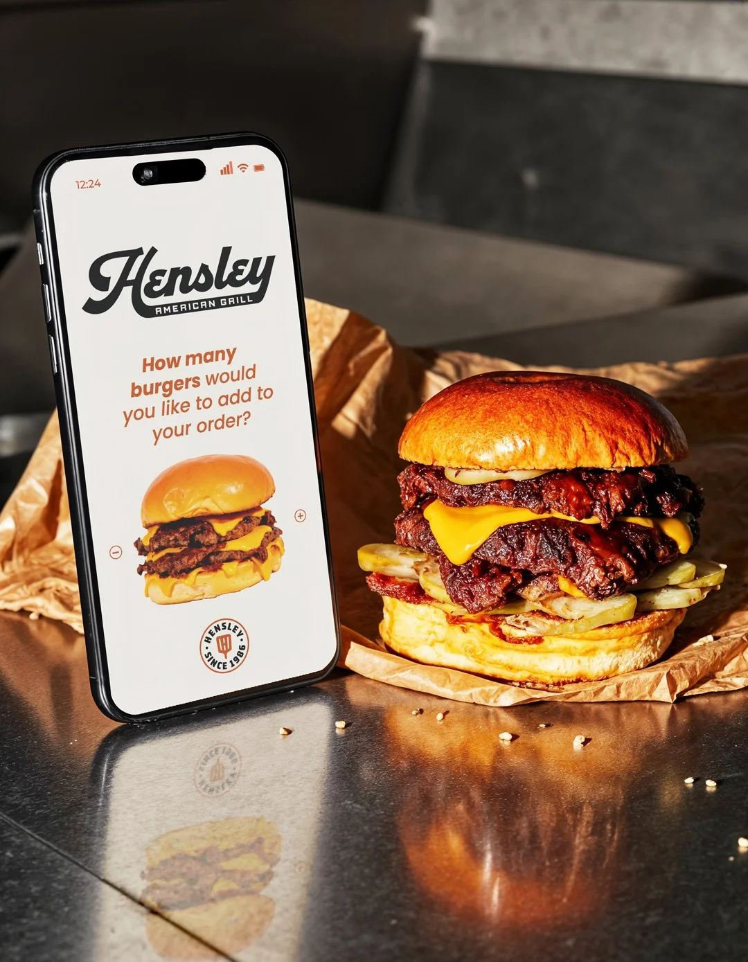 Hensley American Grill mobile app screen with burger photography, badge logo, and order now interface.