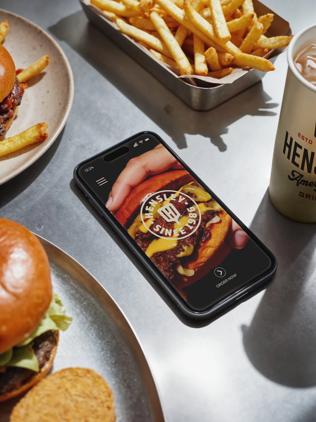 Mobile ordering app mockup for Hensley American Grill shown beside a burger with vintage restaurant branding.