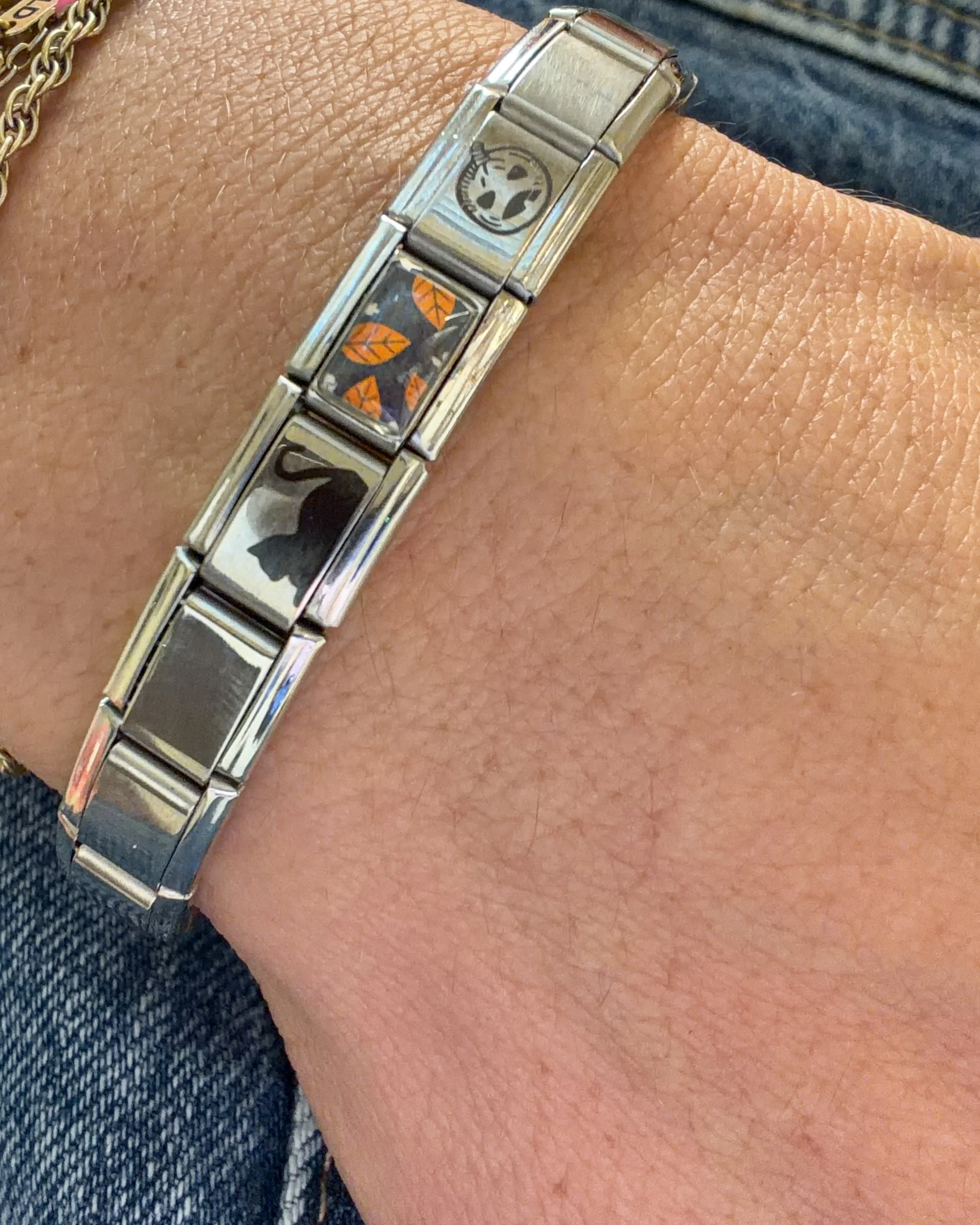 Silver Italian charm bracelet with three Halloween-themed charms featuring a pumpkin, autumn leaves, and a black cat, worn on a wrist.