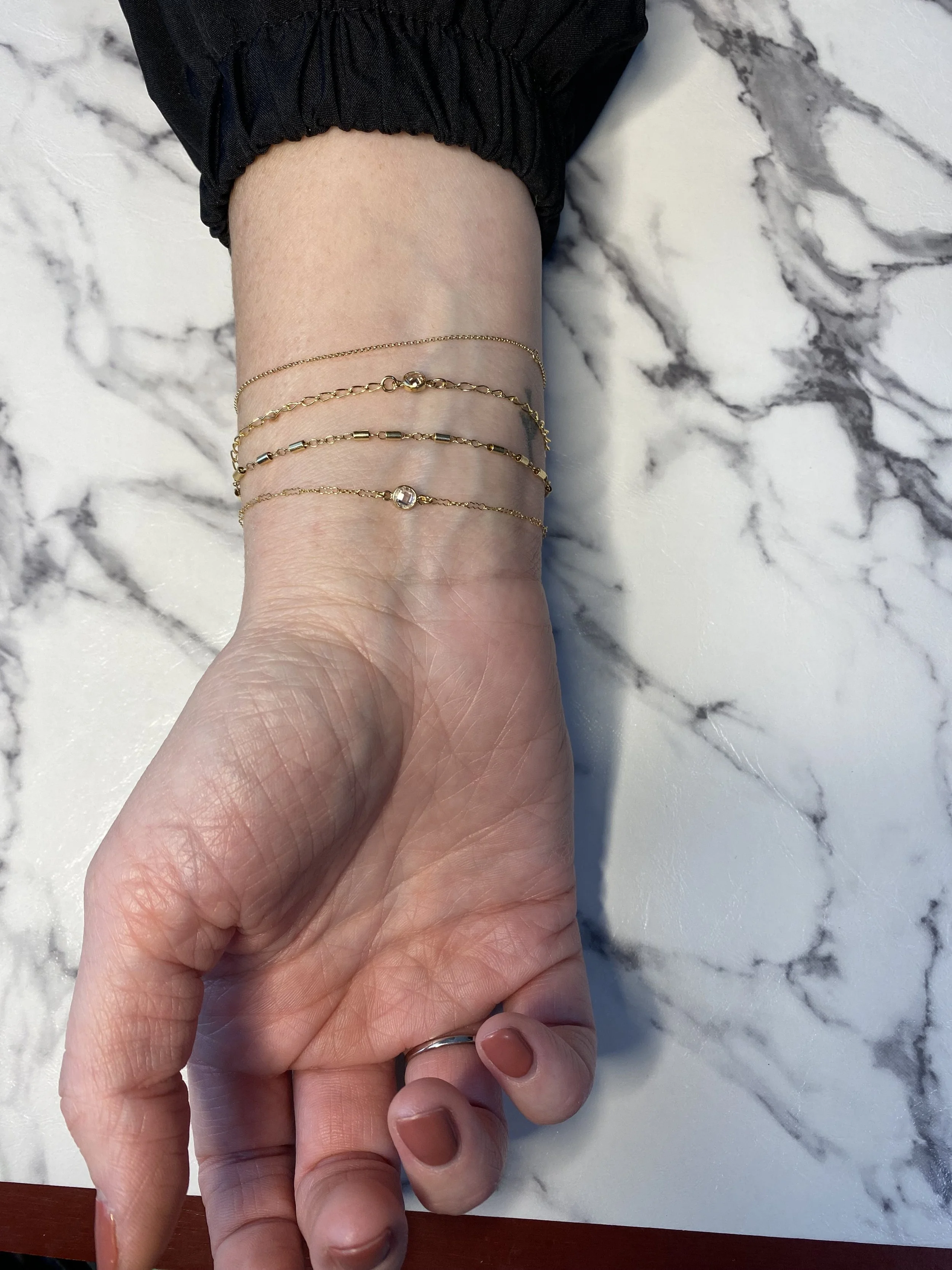 Four gold bracelets on a woman's wrist. Two of the bracelets with diamond charms on them.