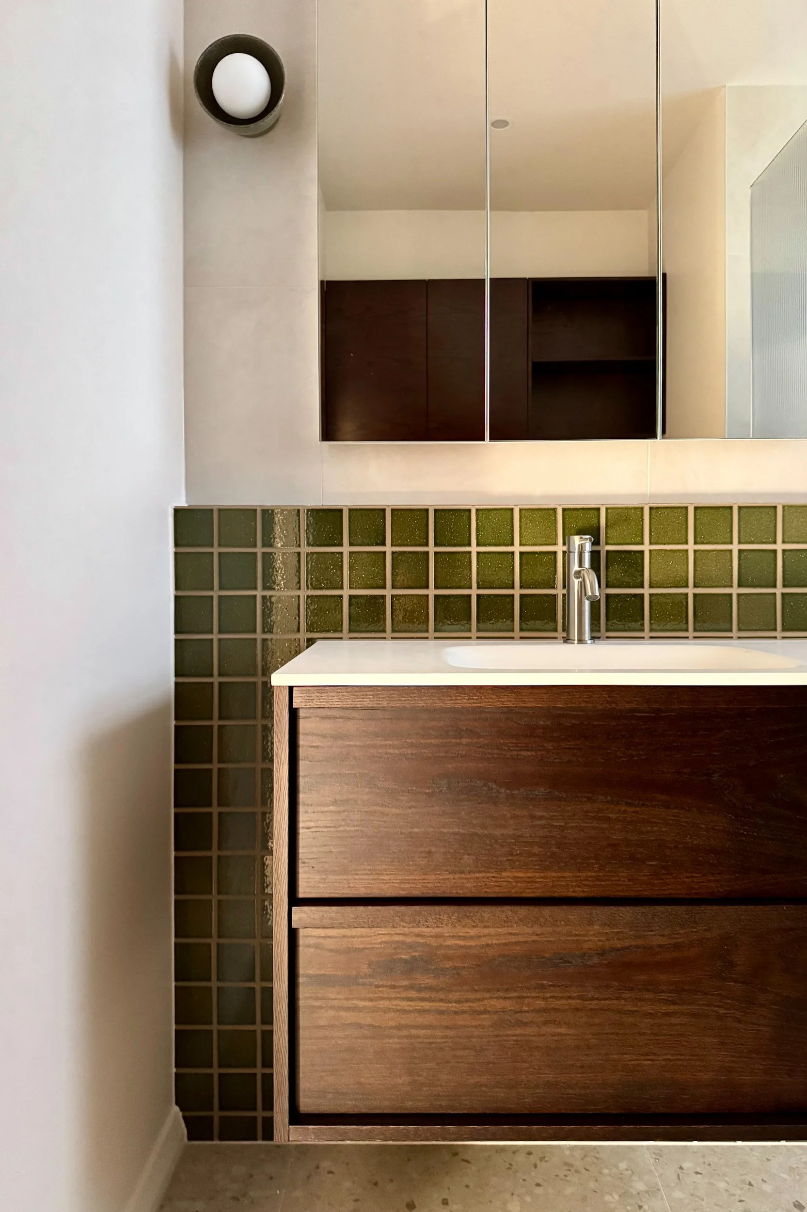 Bathroom vanity with dark wood drawers, tiled backsplash with green glass blocks, and a silver faucet.