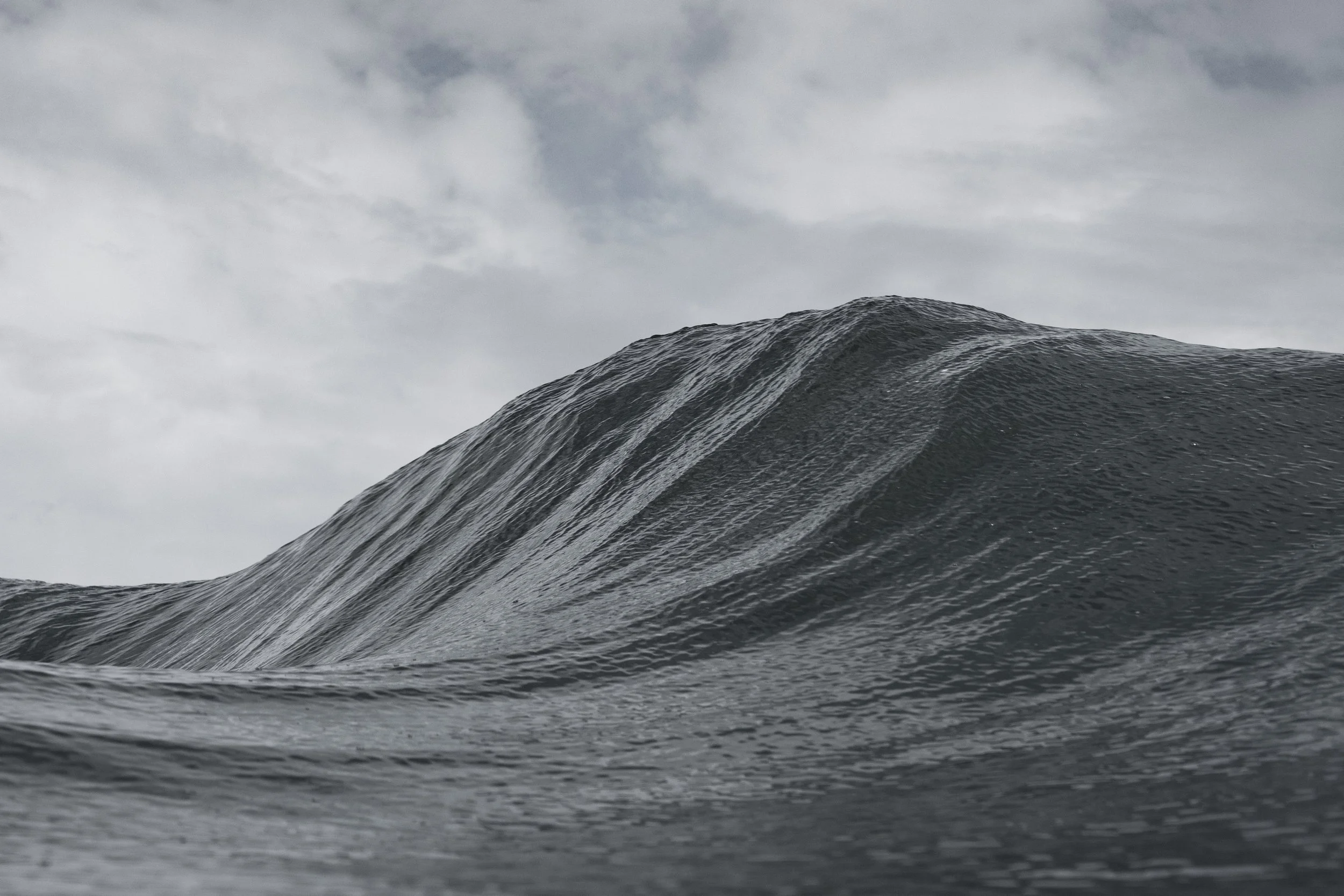 Close-up of a large ocean wave under cloudy sky.