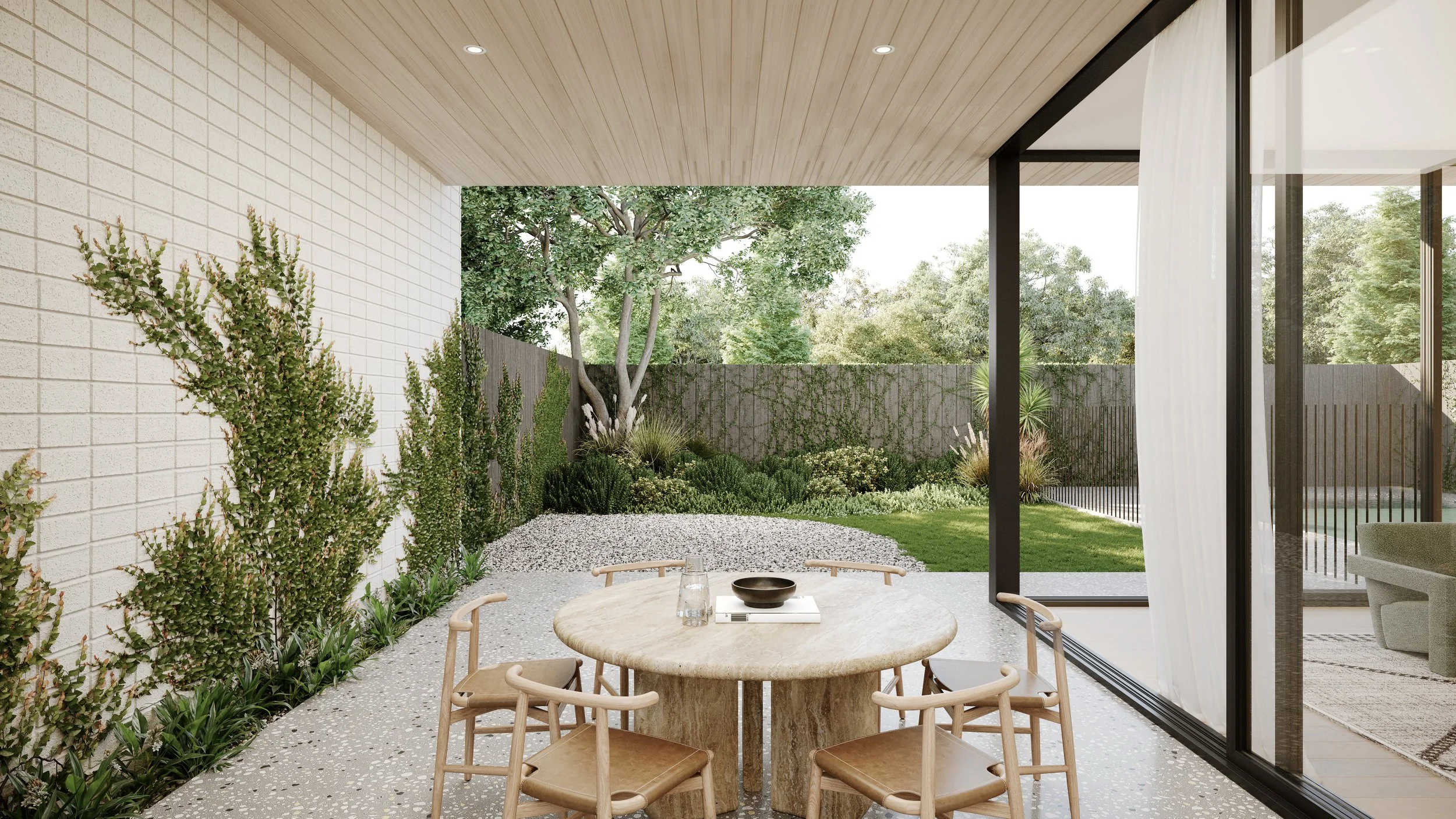 Outdoor patio dining area with a round stone table, six wooden chairs, and a view of a garden with trees, shrubs, and a lawn, separated by a fence and enclosed by a glass wall with sheer white curtains.