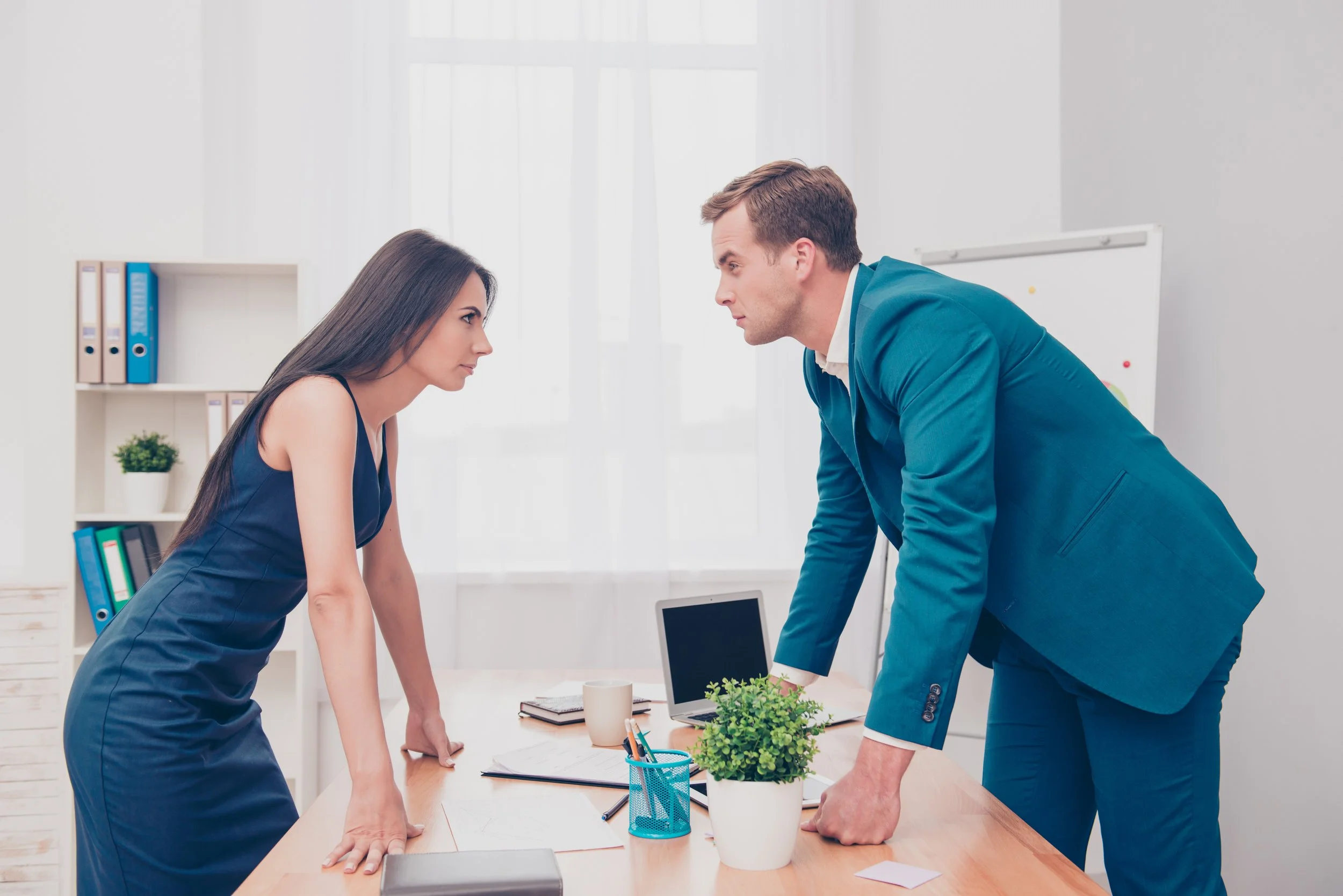 Two office workers, a man and a woman, leaning over a desk in a discussion in a modern office setting.