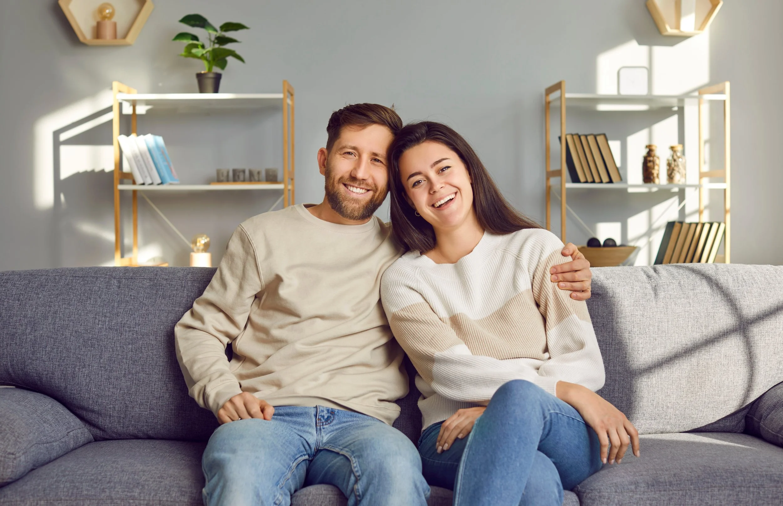Smiling couple sitting on a gray couch in a living room.