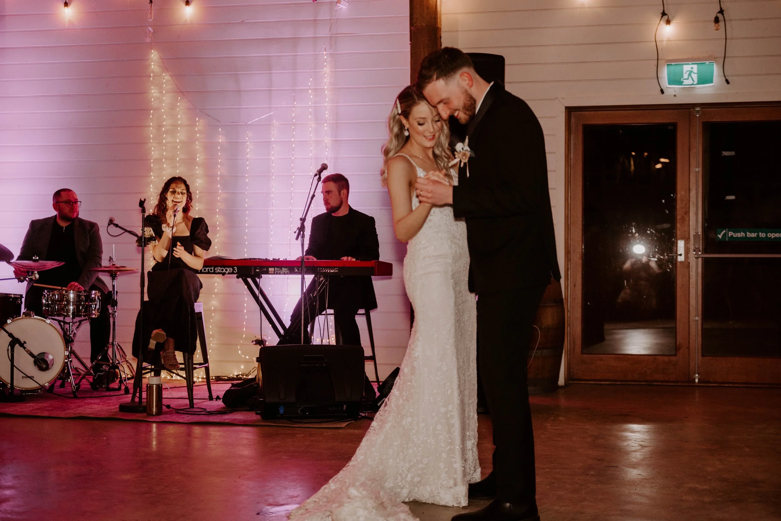 A bride and groom share a dance at their wedding reception, with a live band performing music in the background.