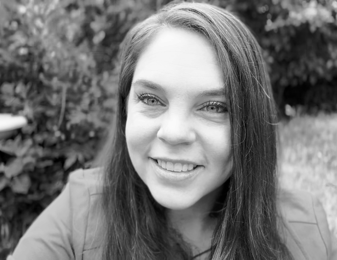 Headshot of Mara Waldruff, a Caucasian, millennial woman with long dark hair, smiling in an outdoor setting