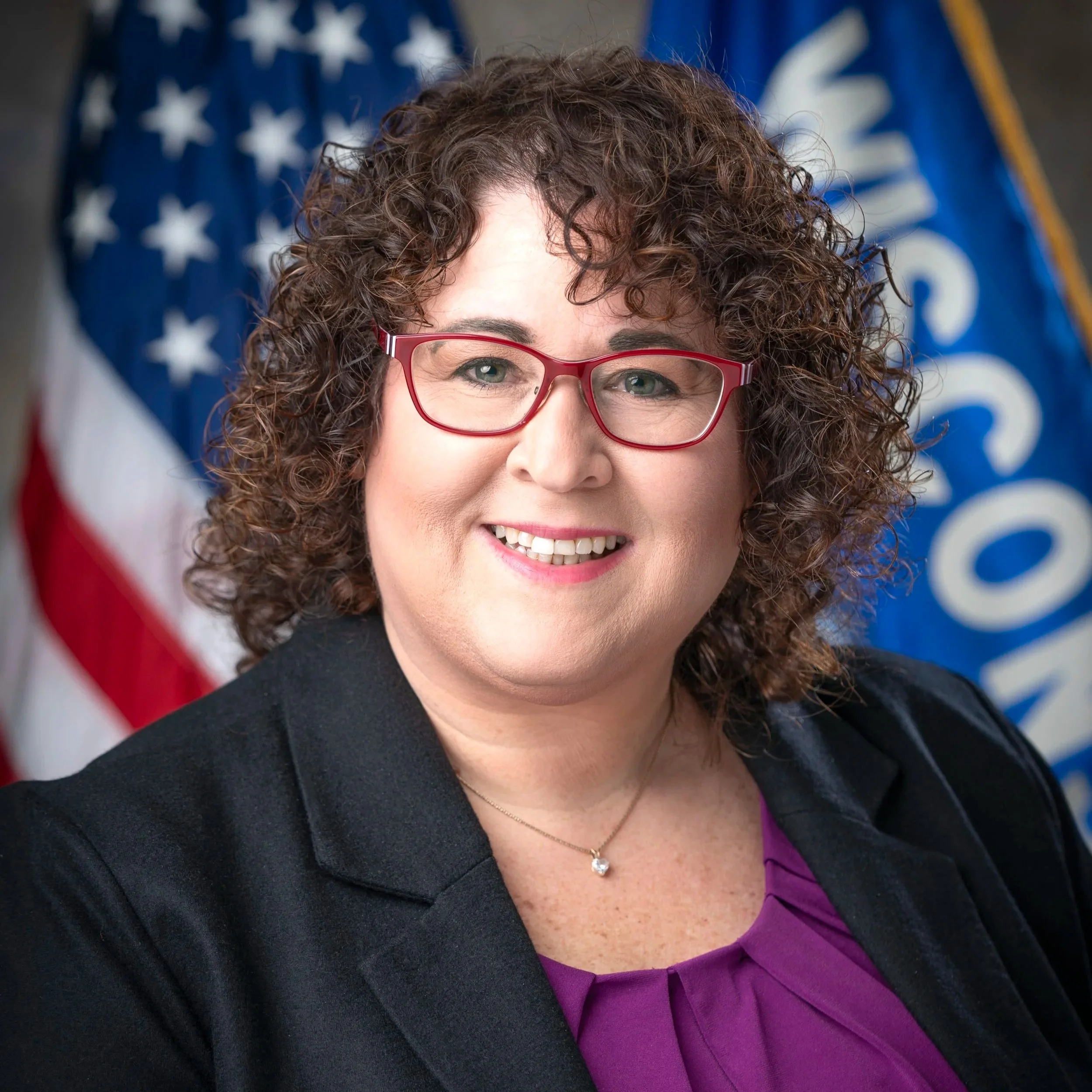 Lisa Subeck poses for a headshot in front of two flags.