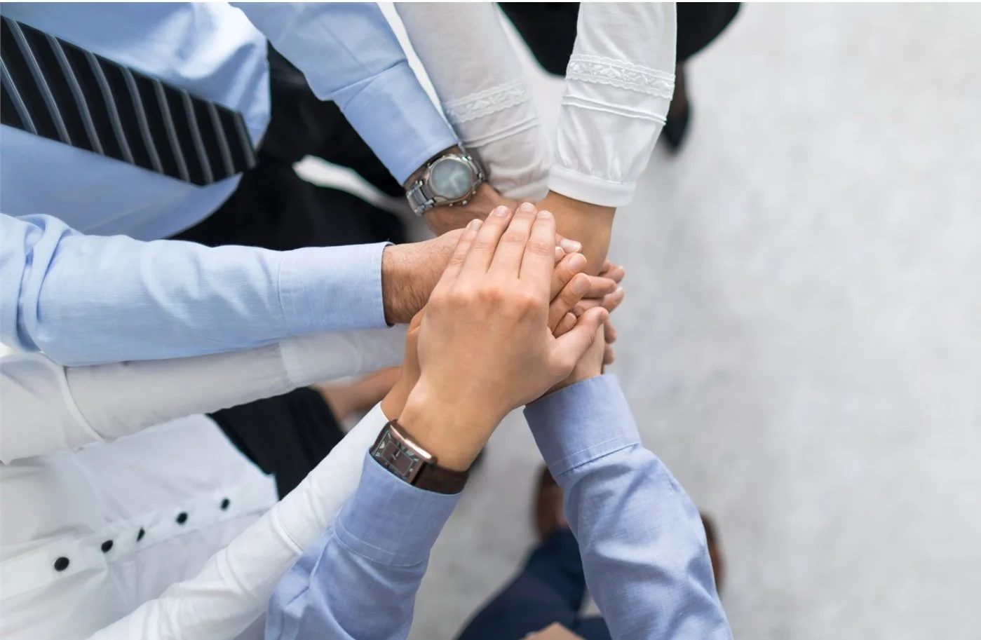 A group of people in professional attire are stacking their hands together in a gesture of teamwork or unity.