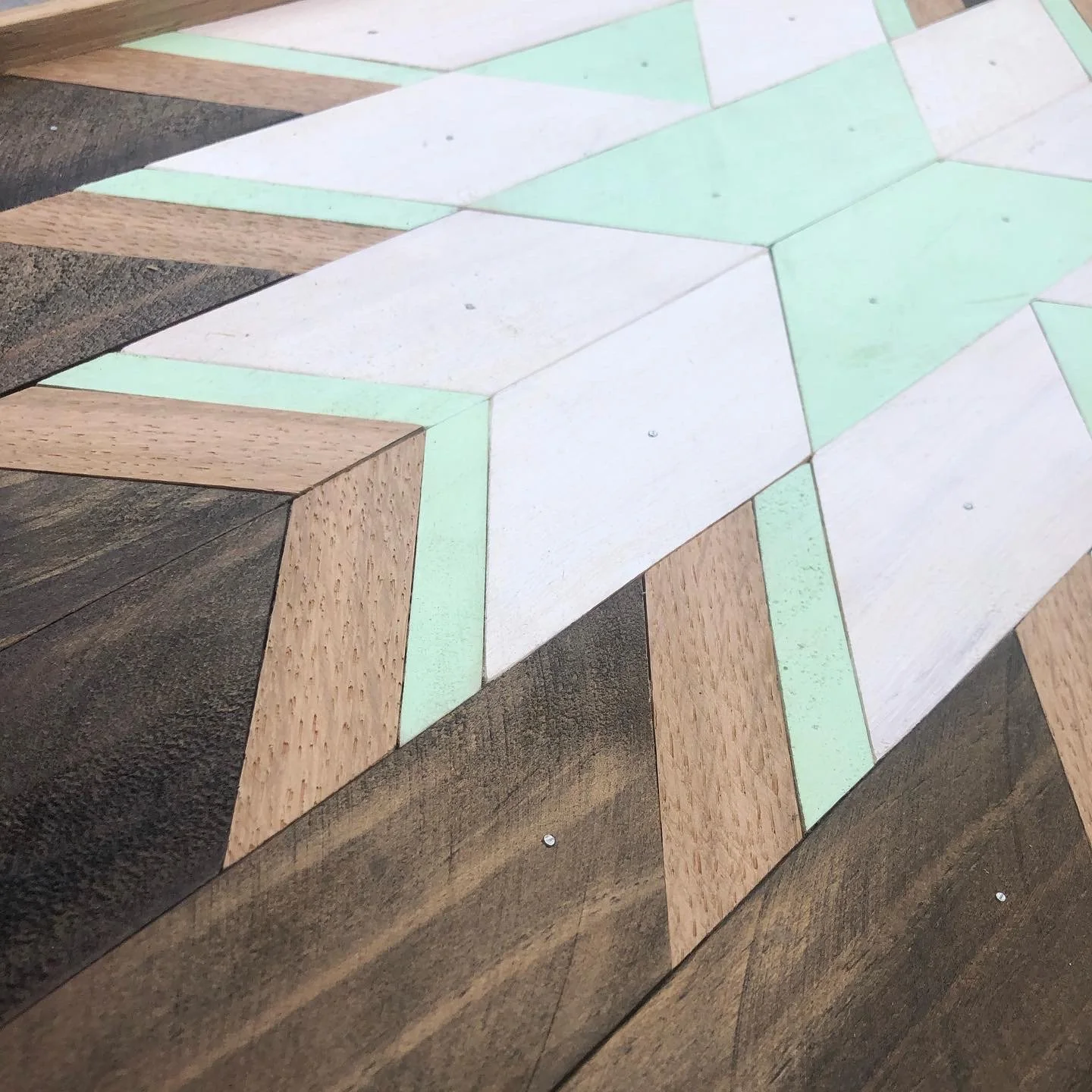 Geometric wooden pattern with alternating light and dark wood tones, featuring green and white accents forming a star shape.