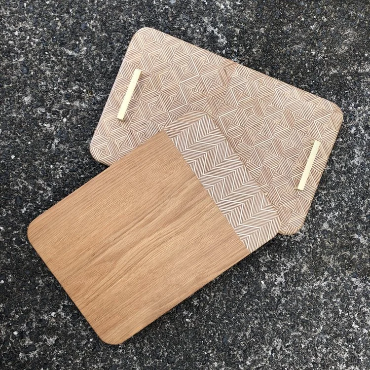 Wooden rectangular cutting boards with geometric patterns on a textured surface.
