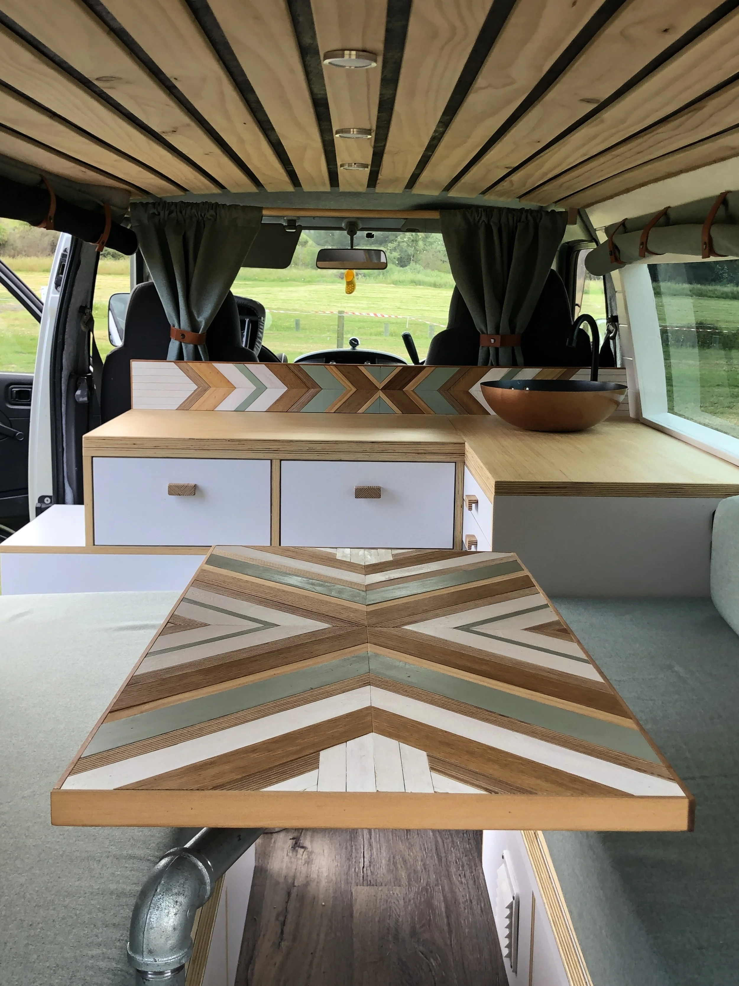 Interior of a camper van with decorative wood paneling, a patterned wooden table, storage drawers, and modern decor.