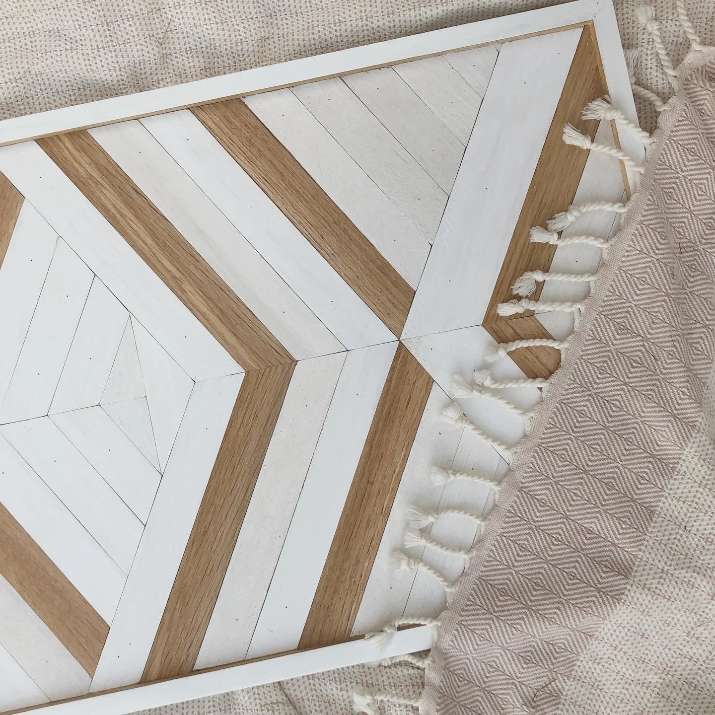 Wooden wall art with geometric pattern on a textured fabric background.