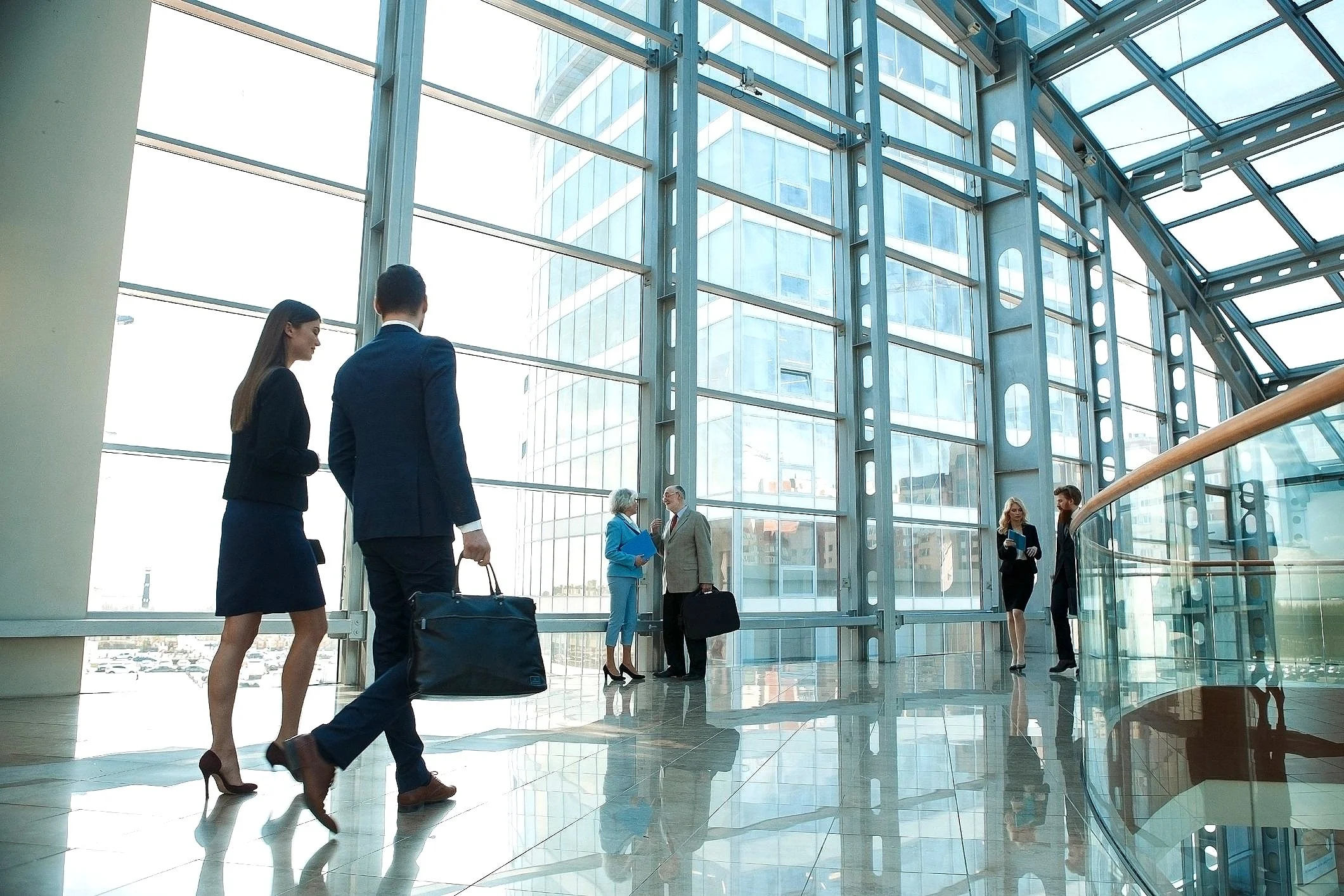 Personas vestidas formalmente caminando por un pasillo moderno con grandes ventanales.