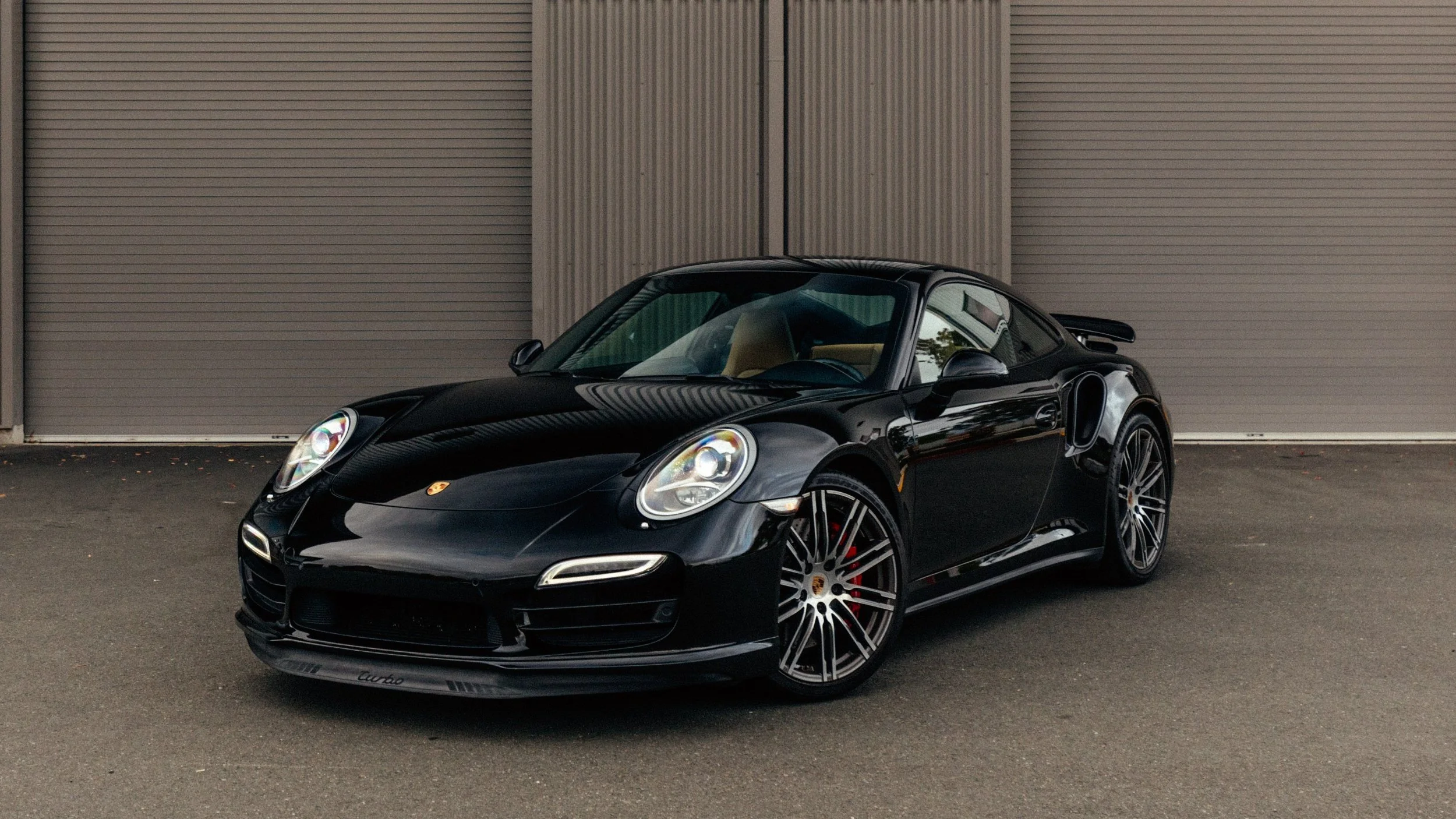 Black Porsche sports car parked outside in front of metal garage doors.