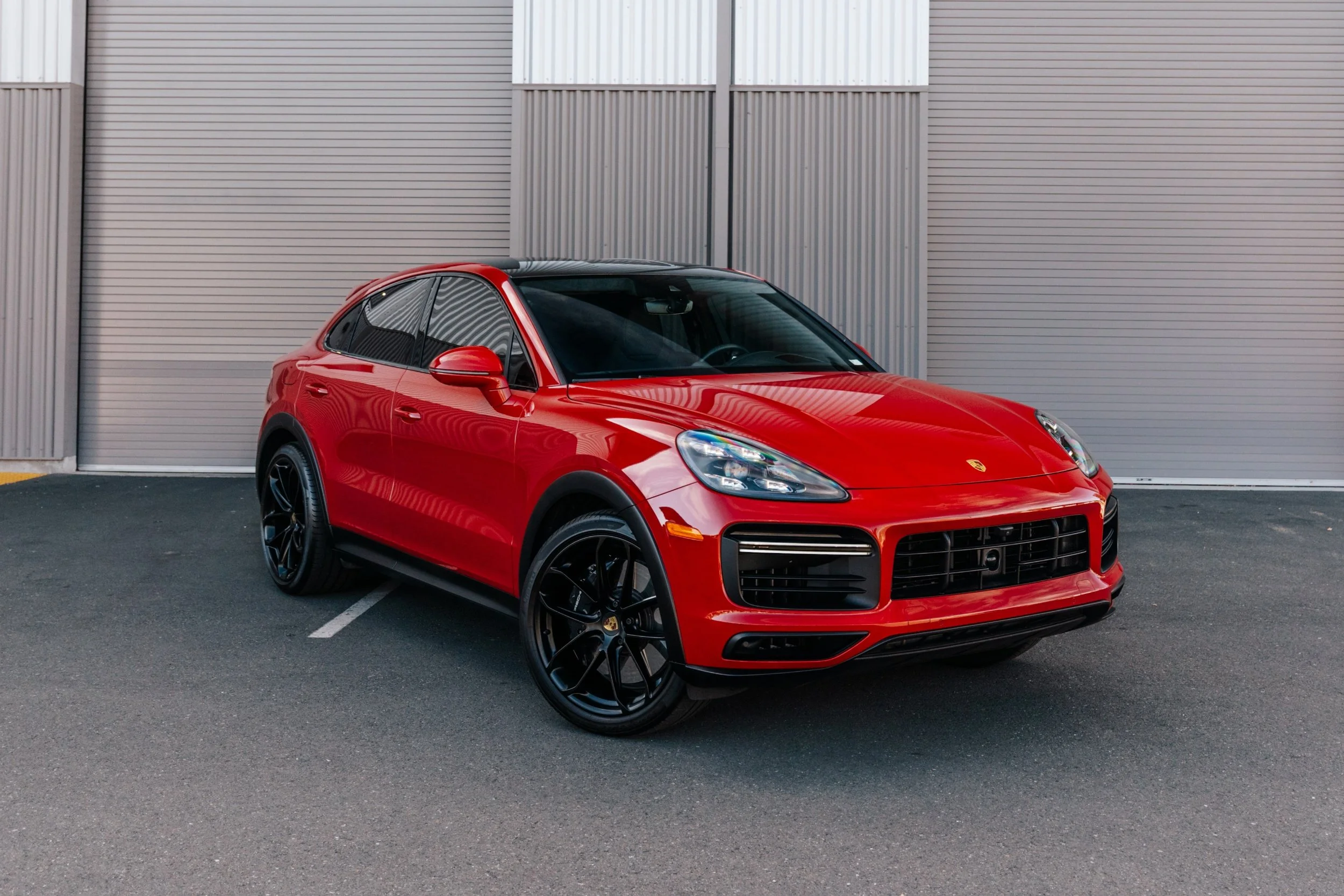 Red luxury SUV parked outdoors against a corrugated metal wall.