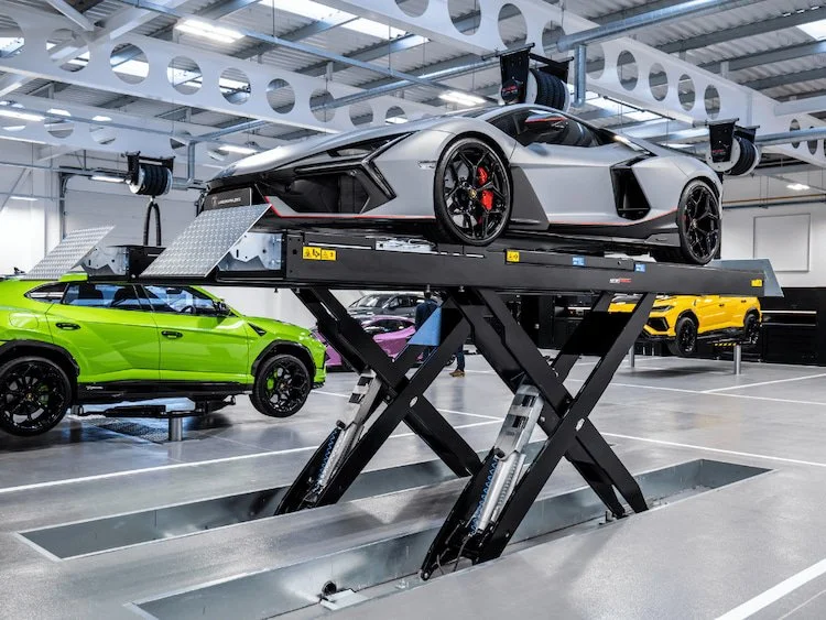 Silver sports car raised on a scissor lift in an automotive workshop.