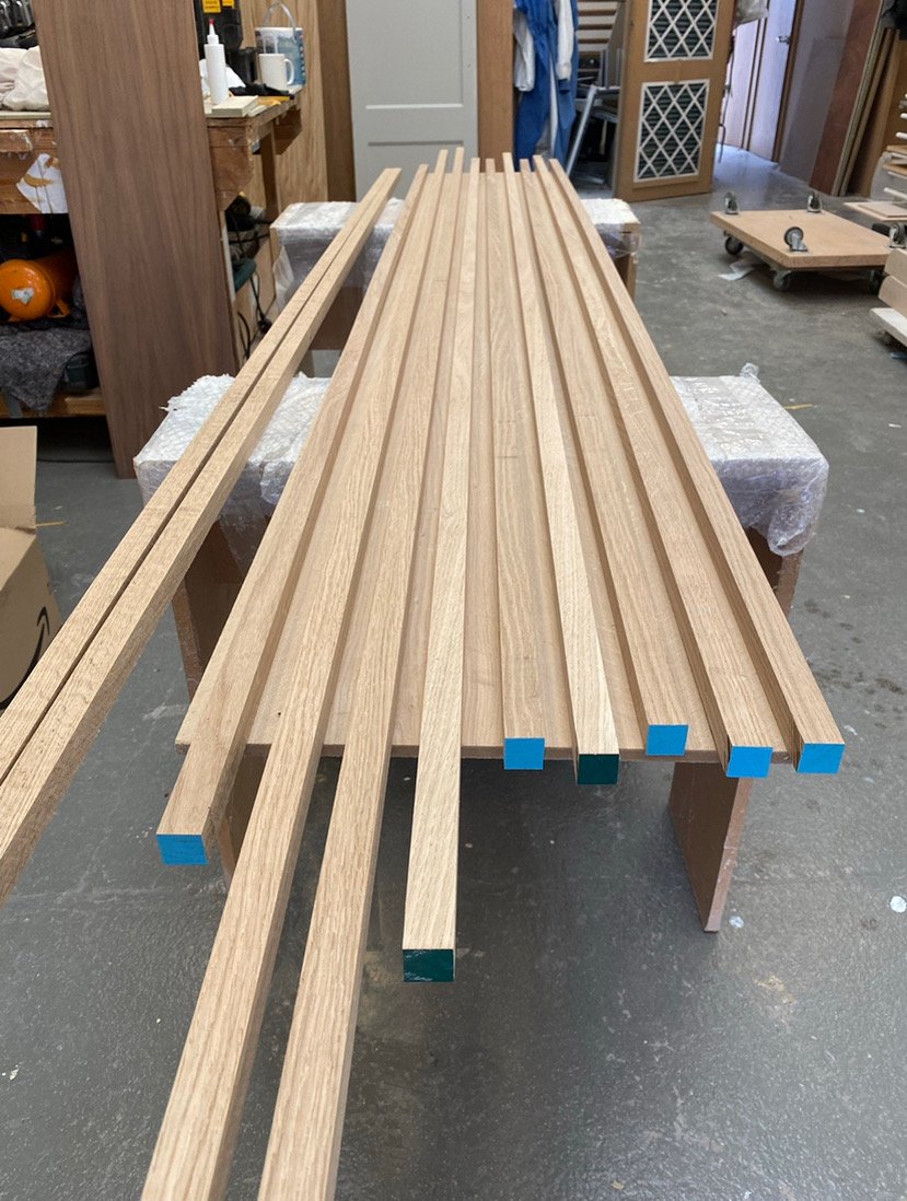 Wooden slats with colored ends laid out on a workbench in a woodworking shop.