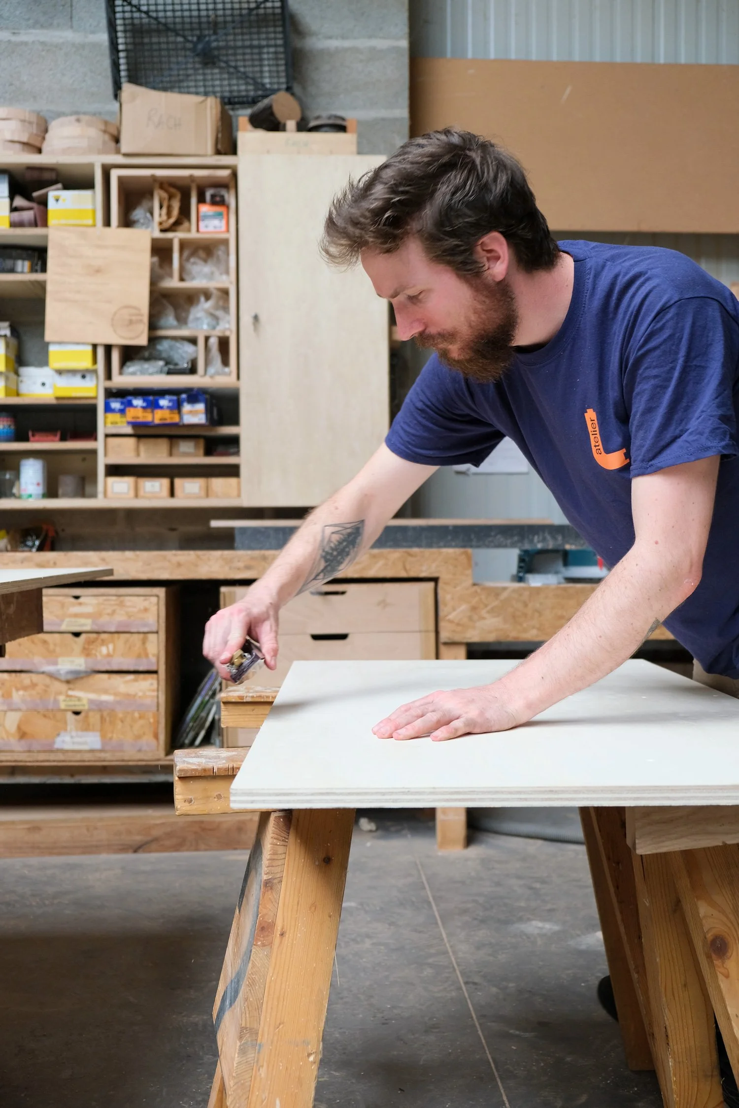 Un homme travaille dans un atelier de menuiserie, il utilise un outil pour couper ou façonner une planche en bois sur un établi en bois.