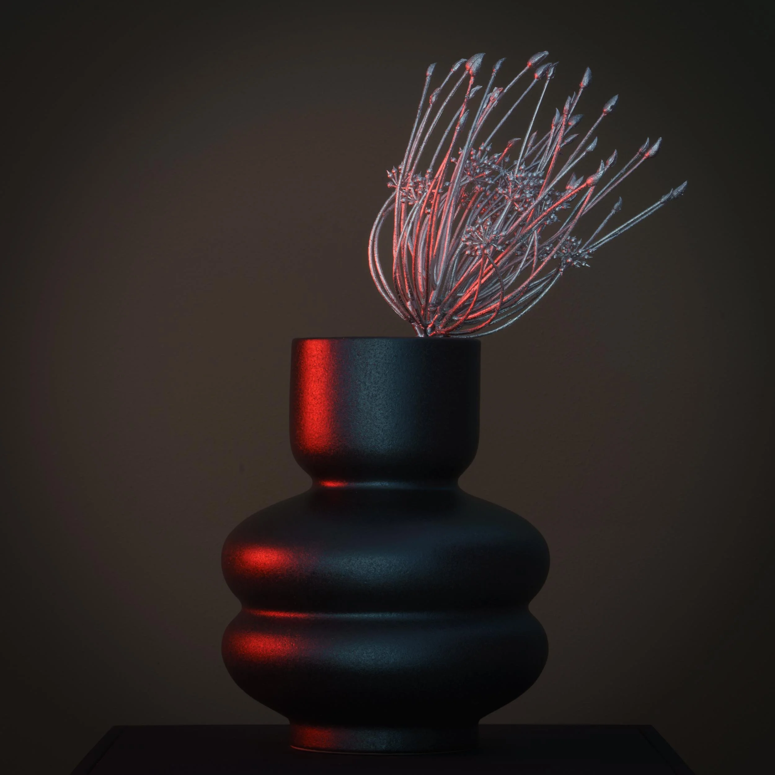 Schwarze Vase mit rotem und blauen Licht, enthält eine abstrakte, leuchtende Skulptur aus feinen, gewundenen Metallstäben.