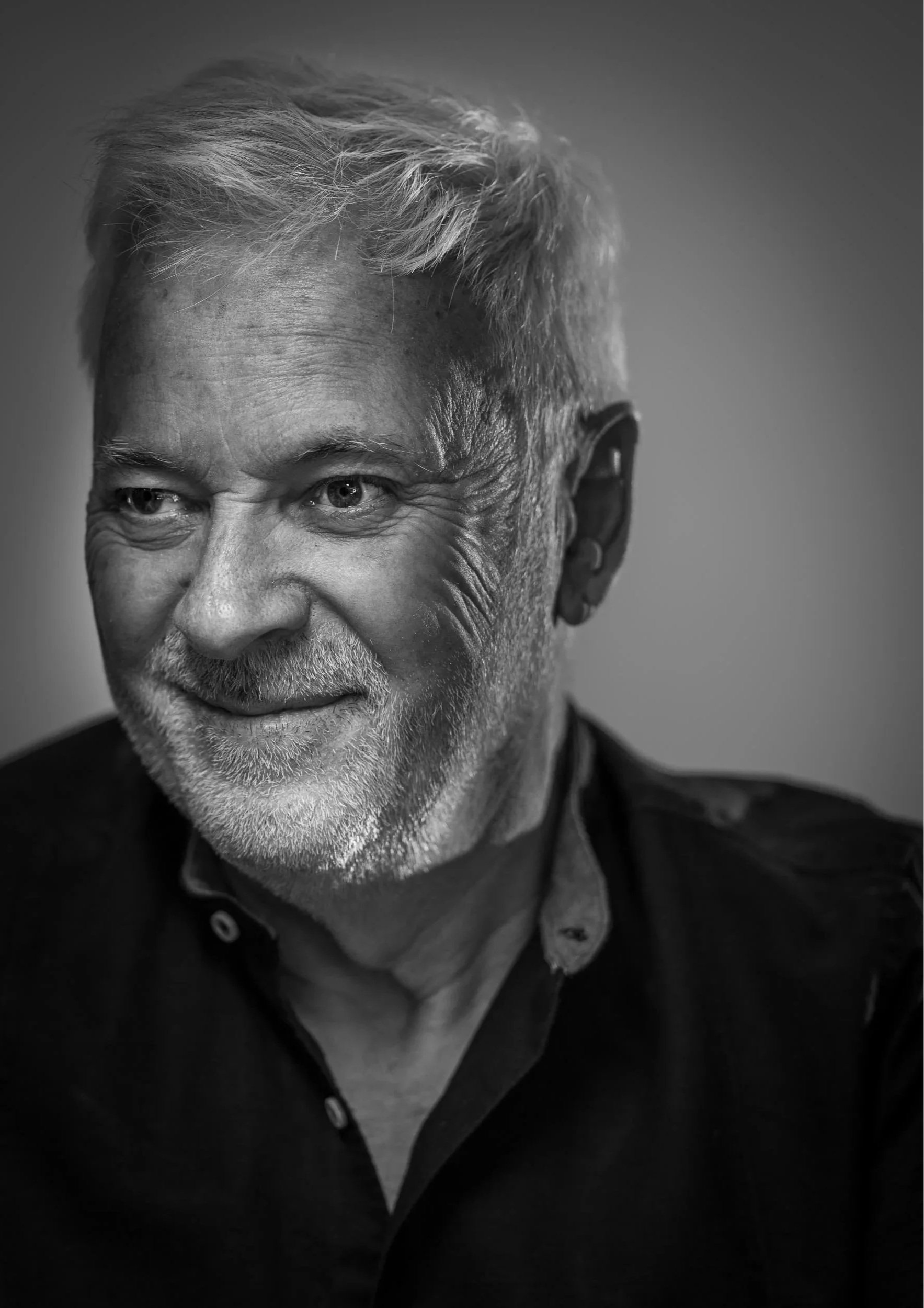 Schwarz-Weiß-Porträt eines lächelnden Mannes mit weißen Haaren und Bart, trägt eine dunkle Jacke