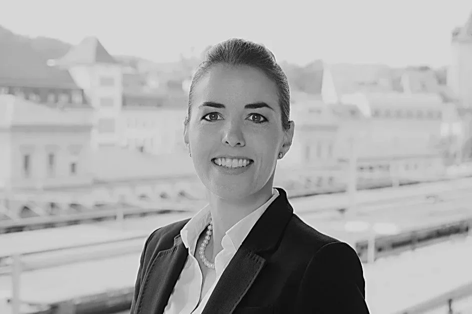 professionelle Frau mit blauer Bluse und dunklem Blazer vor Stadtblick.