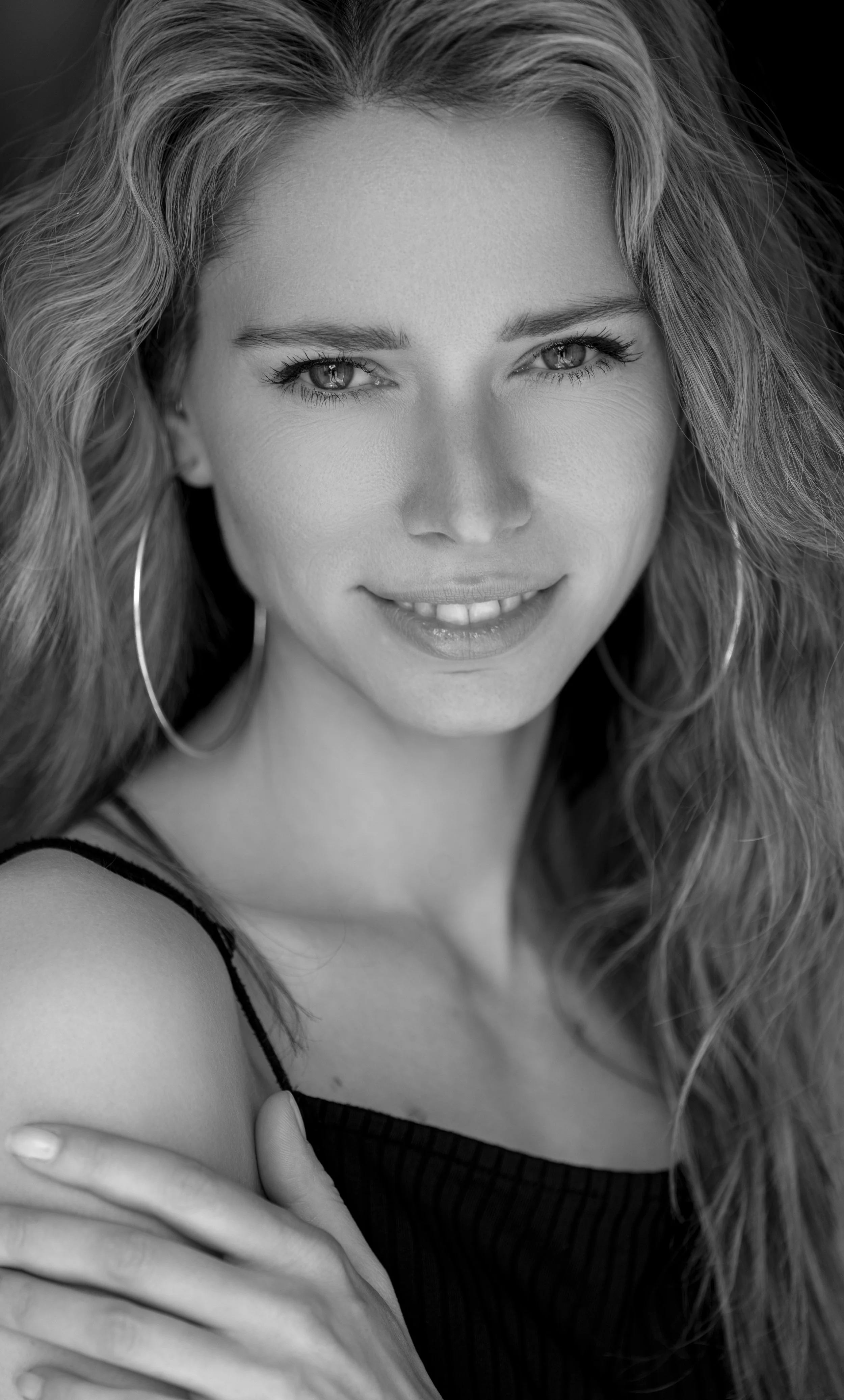 Schwarz-weiß-Fotografie eines Lächelns einer jungen Frau mit lockigem Haar, die einen Arm über die Schulter gelegt hat.