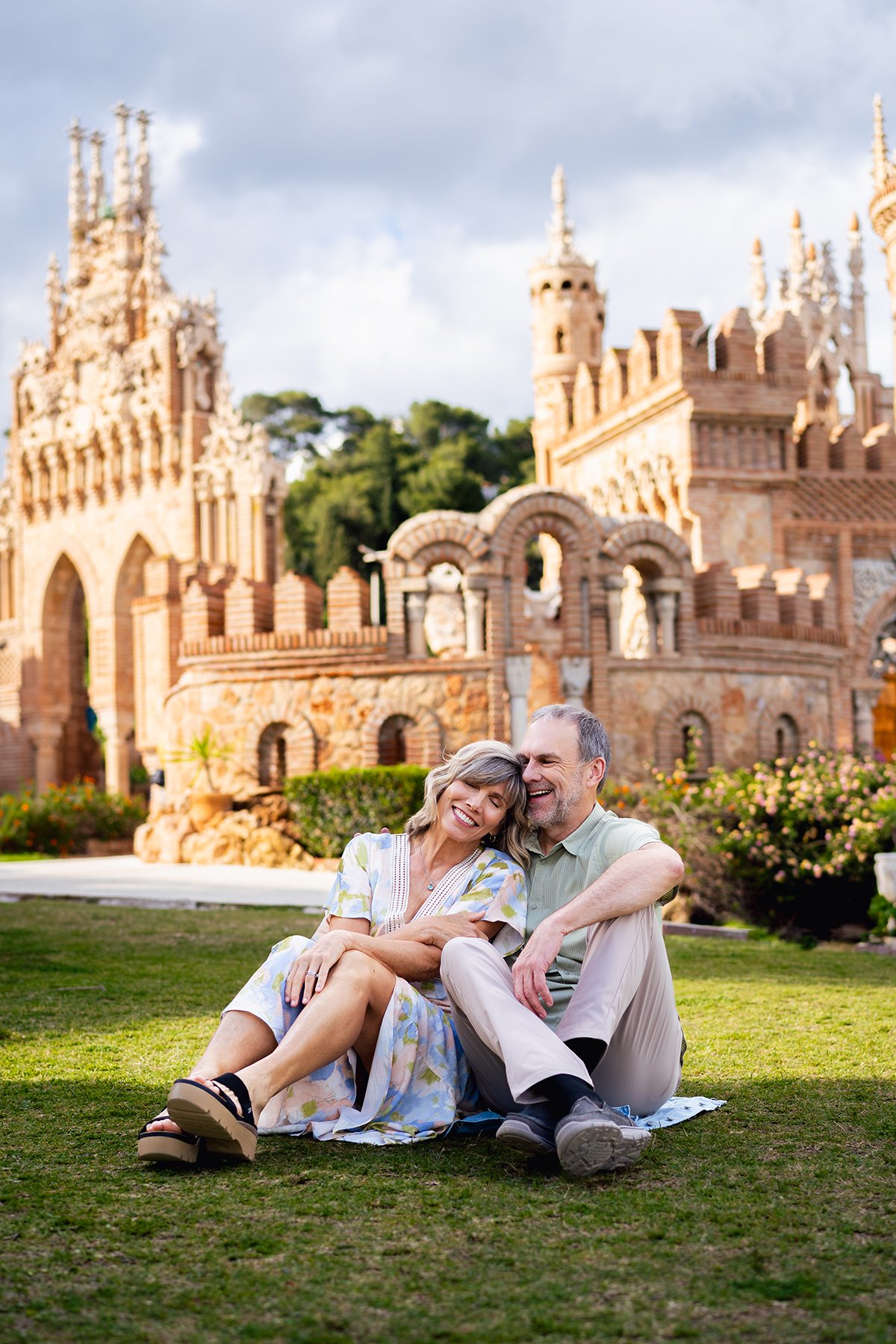 A happy family posing on stone steps outdoors, featuring a woman in white pants, a man in a patterned shirt, and a child in a white t-shirt.