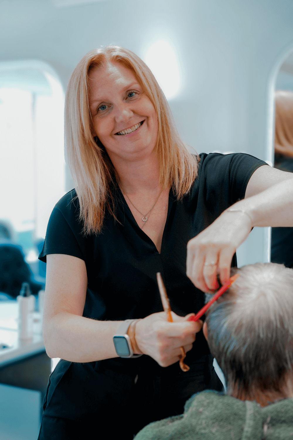 A smiling woman providing a haircut to an elderly person in a salon or barbershop.