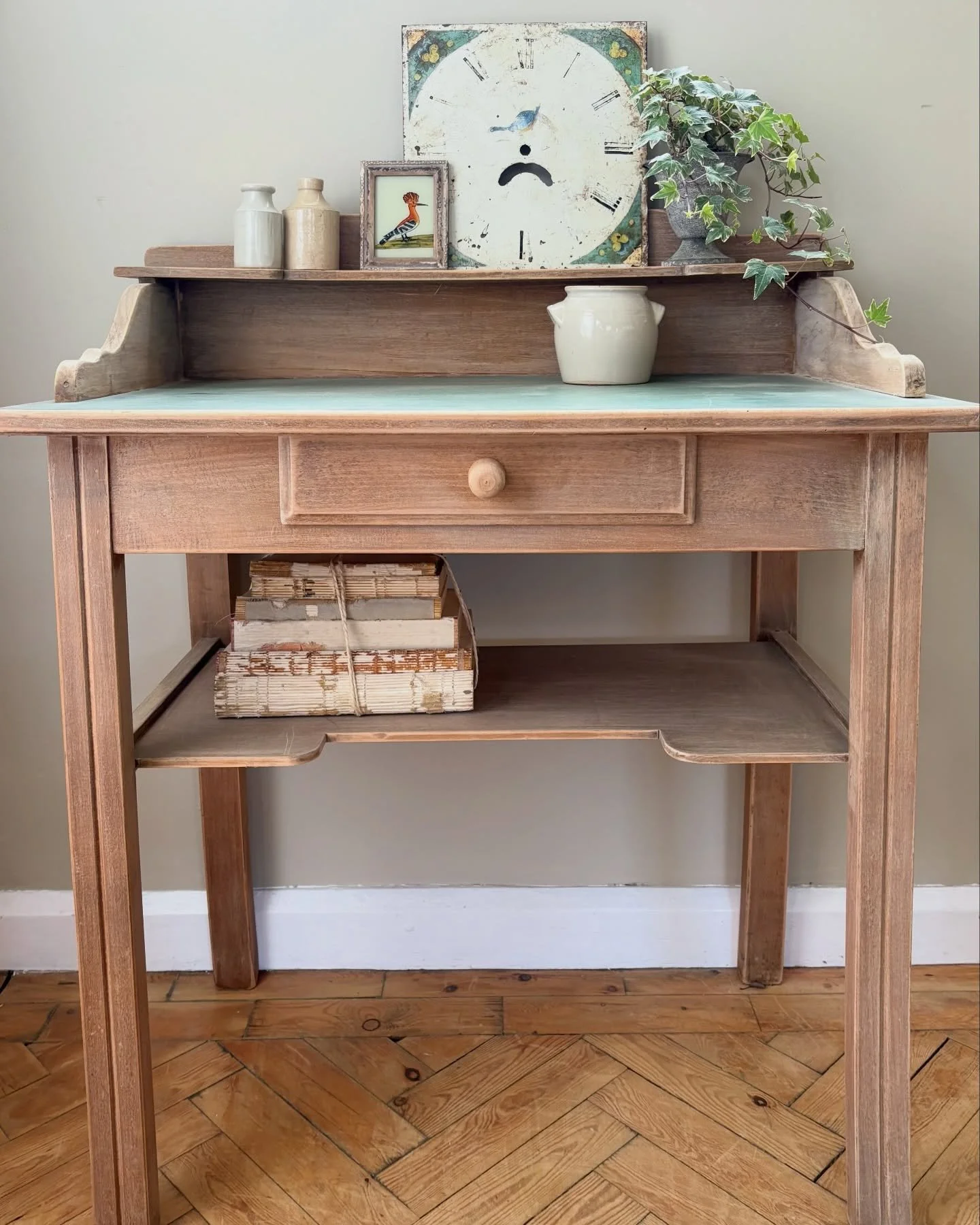 A fabulous mid-century vintage desk in a light timber tone with a beautifully distressed blue-green top. This solidly constructed desk features a single drawer and a handy low-level shelf, perfect for storing books or papers, adding to its versatile 