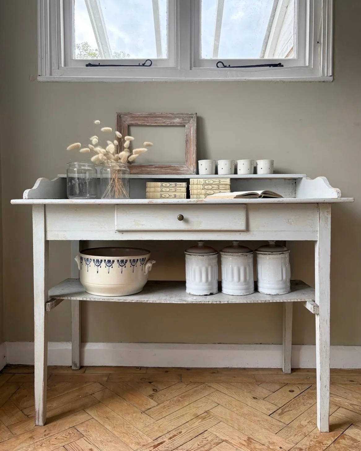 A beautiful vintage French painted washstand, softly layered in neutral tones.

Predominantly pale grey, with warmer shades gently peeking through give this piece a wonderfully aged and quietly timeworn feel. An original brass handle adorns the worki