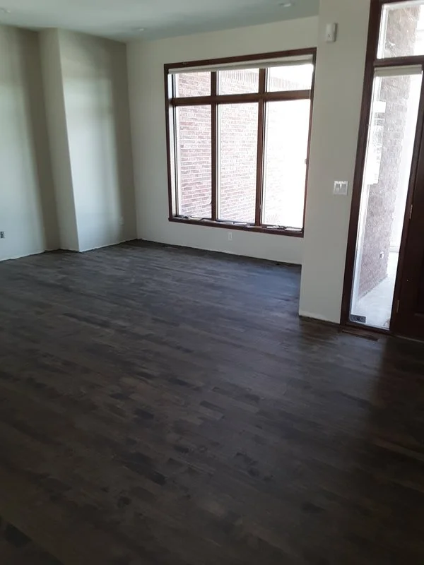Empty room with dark hardwood floors, large window, white walls, and a glass door.