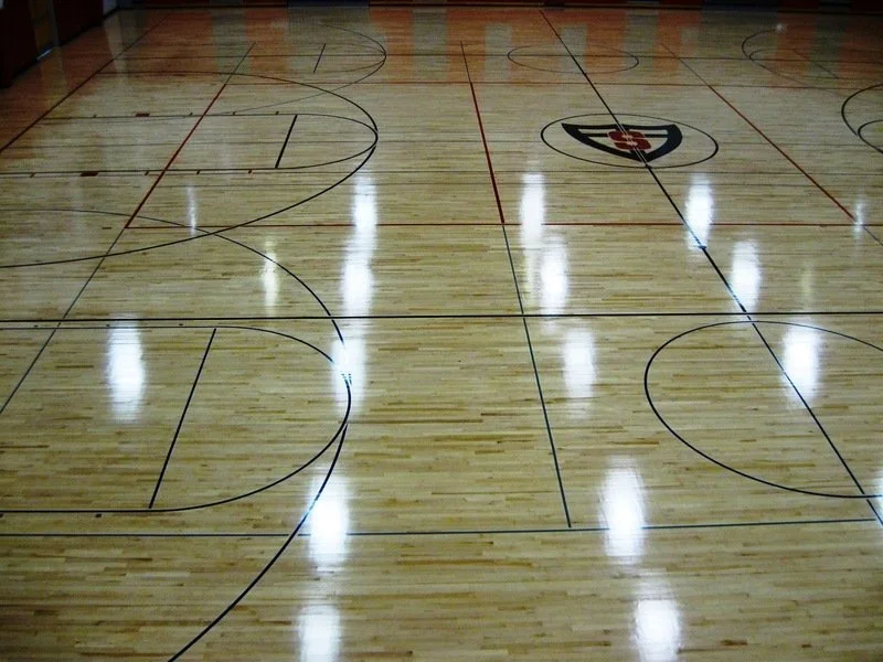Indoor basketball court with wooden flooring and court markings.