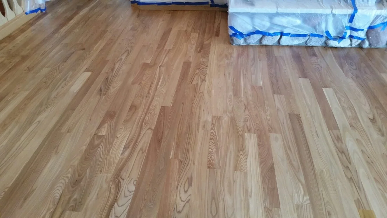 Newly installed light hardwood floor with a wrapped stone fireplace in the background.