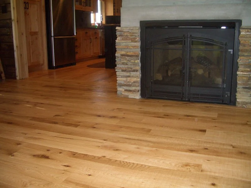 Interior of a room with hardwood flooring, a stone fireplace, and a stainless steel refrigerator.