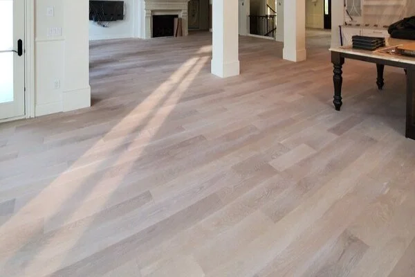 Large room with light wood flooring, columns, a table, and a fireplace in the background.