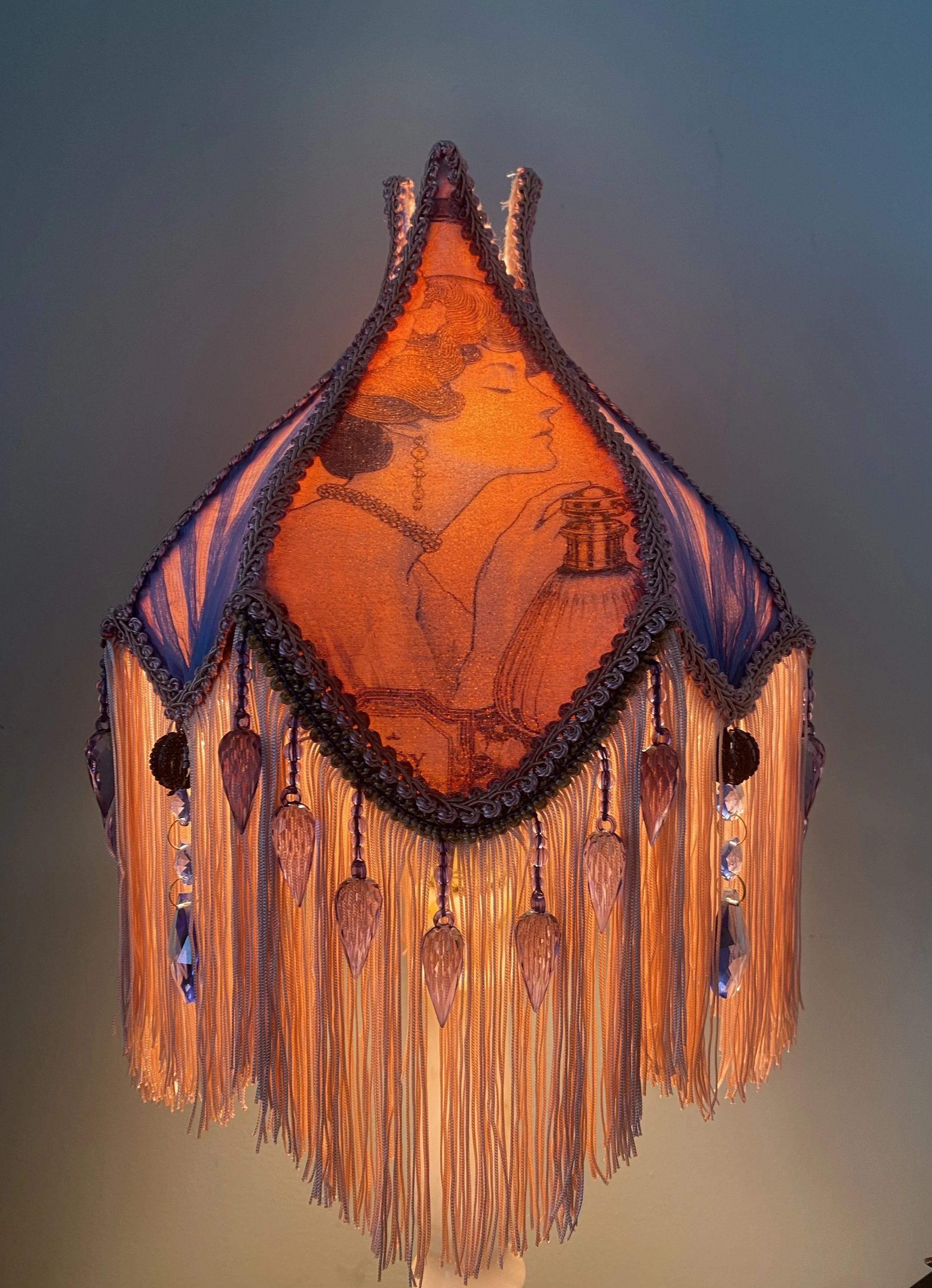 Decorative hanging lamp with intricate fabric and beadwork, featuring an image of a woman holding a perfume bottle.