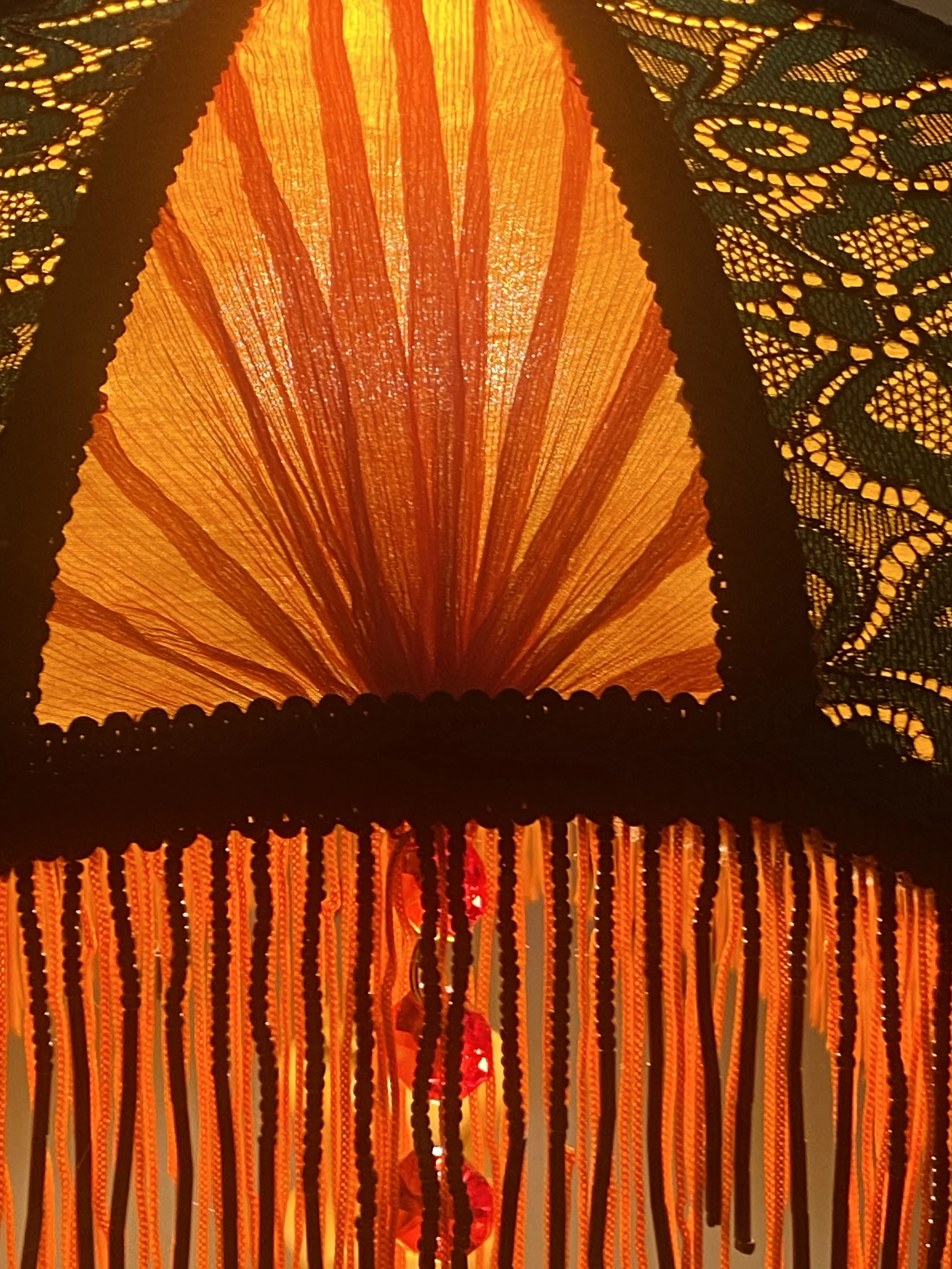 Art deco fringed lampshade in a crescent moon shape, orange silk, green and black lace, scarlet pleated panels , lit up pleated detail