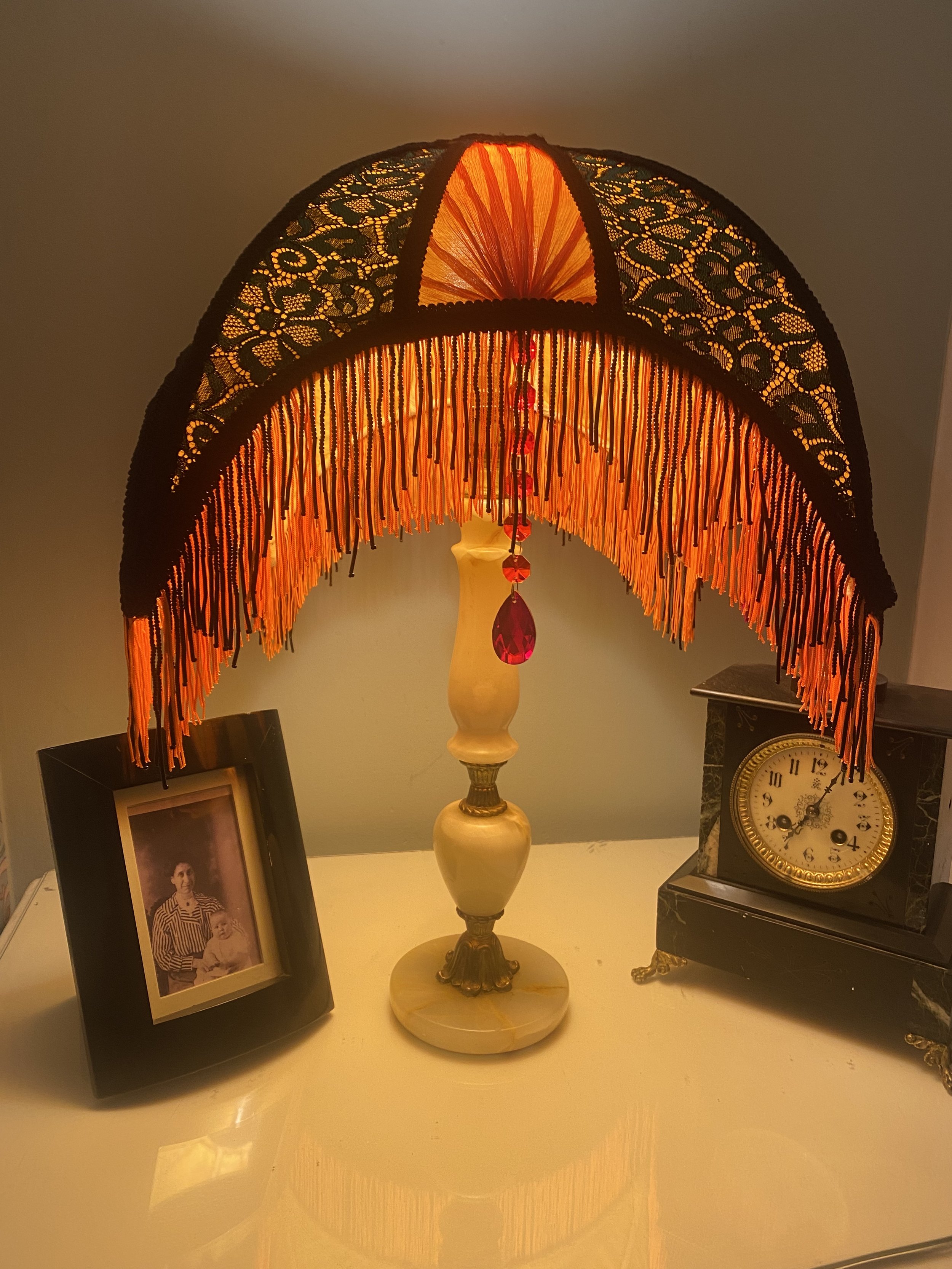 Art deco fringed lampshade in a crescent moon shape, orange silk, green and black lace, scarlet pleated panels , lit up