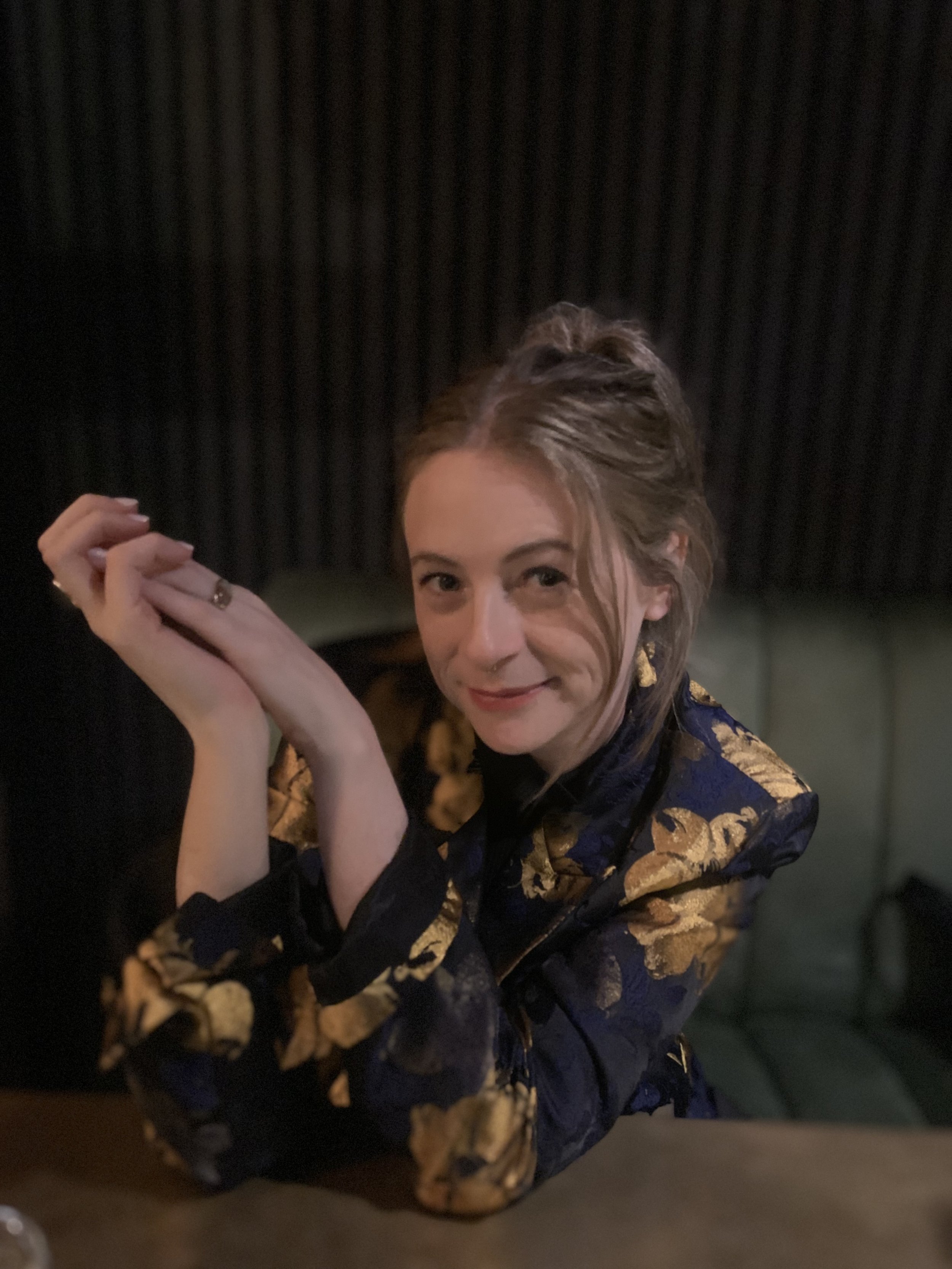 Tina sitting on a green leather couchette in an oriental top smiling