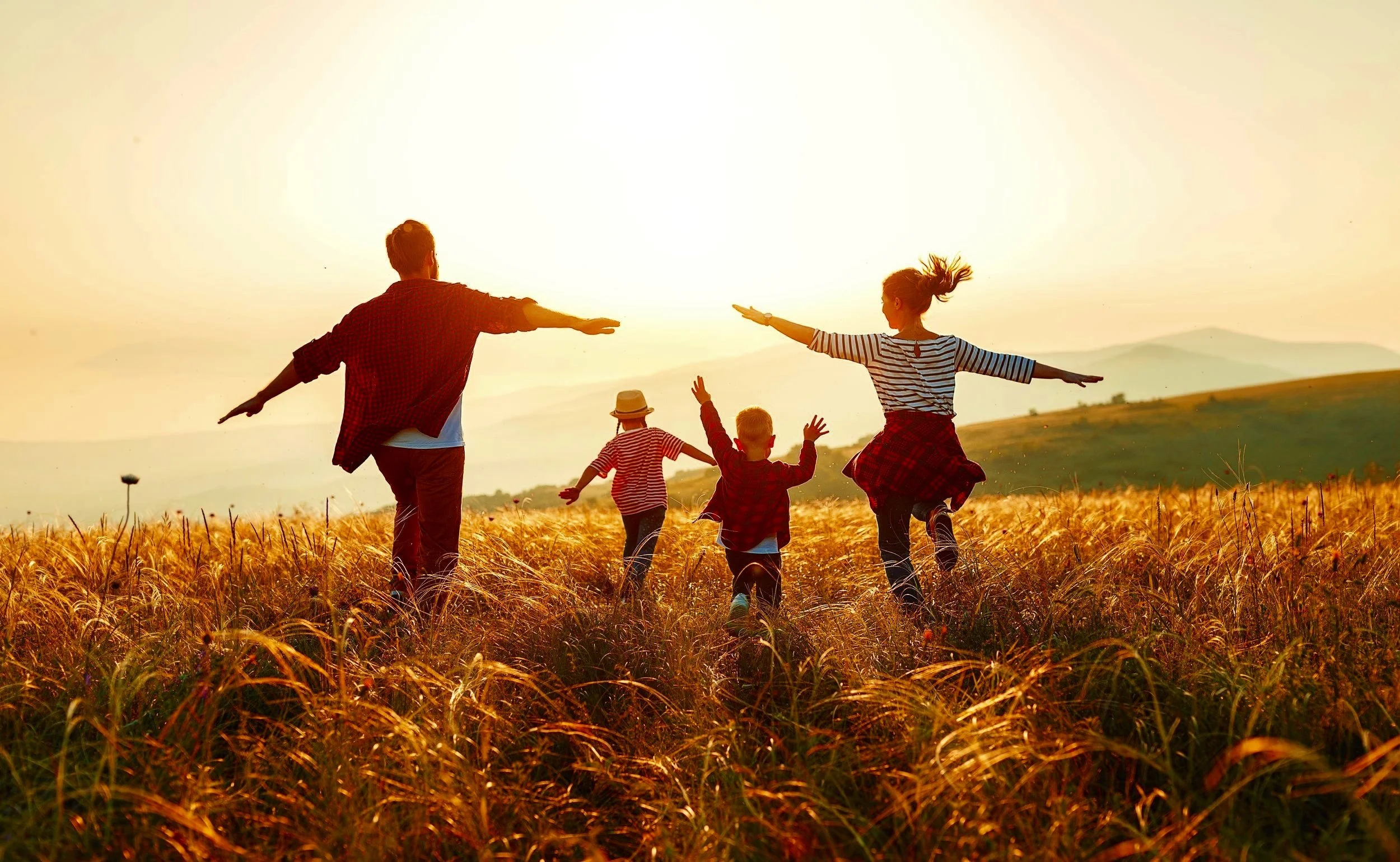 A family running and playing in a field of tall golden grass during sunset, healed after trauma therapy at Counseling and Nature Therapy Center in Frisco, TX.