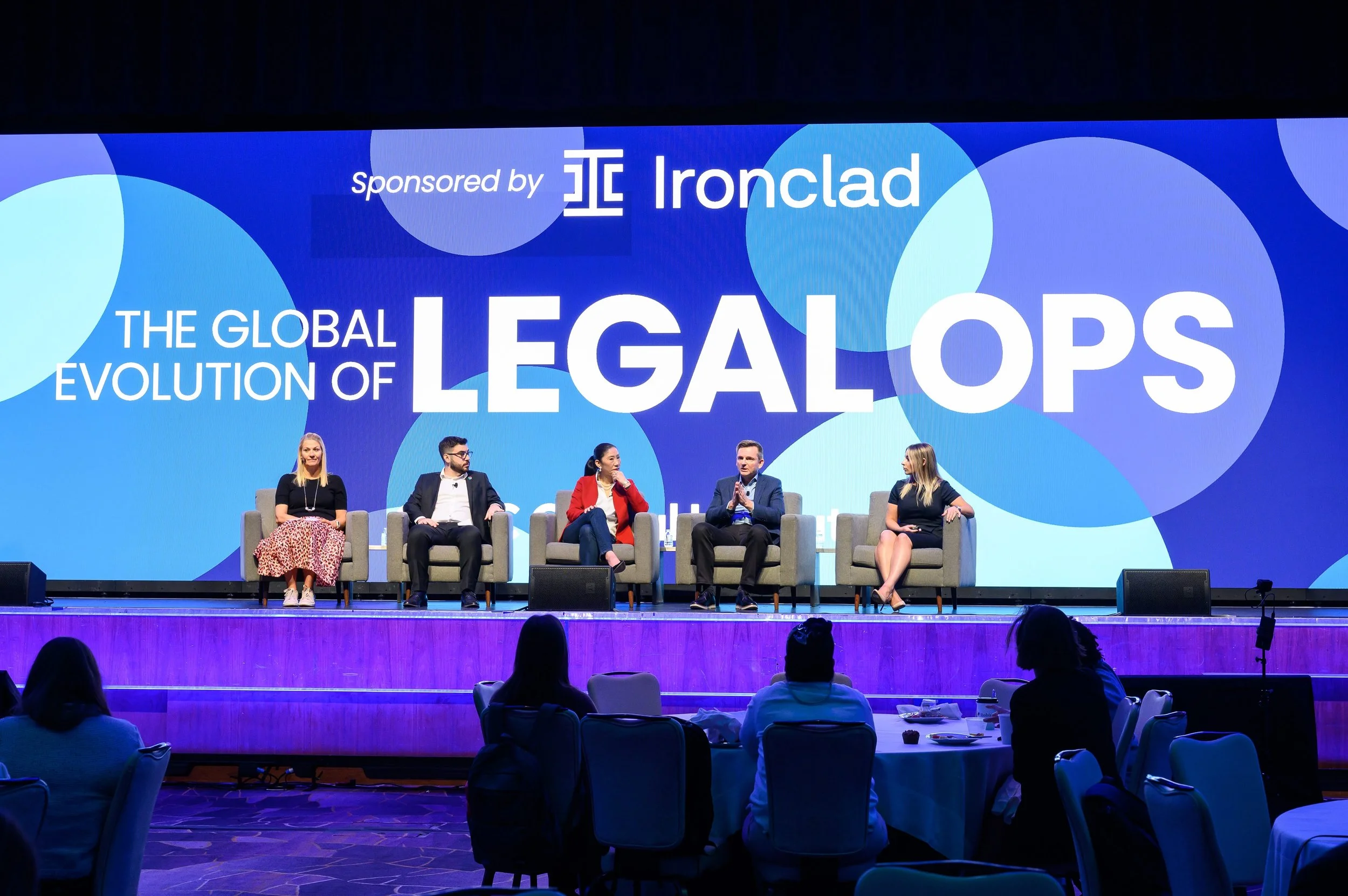 Five people sitting on stage at a panel discussion titled 'The Global Evolution of Legal Ops,' sponsored by Ironclad. Audience members are visible in the foreground.