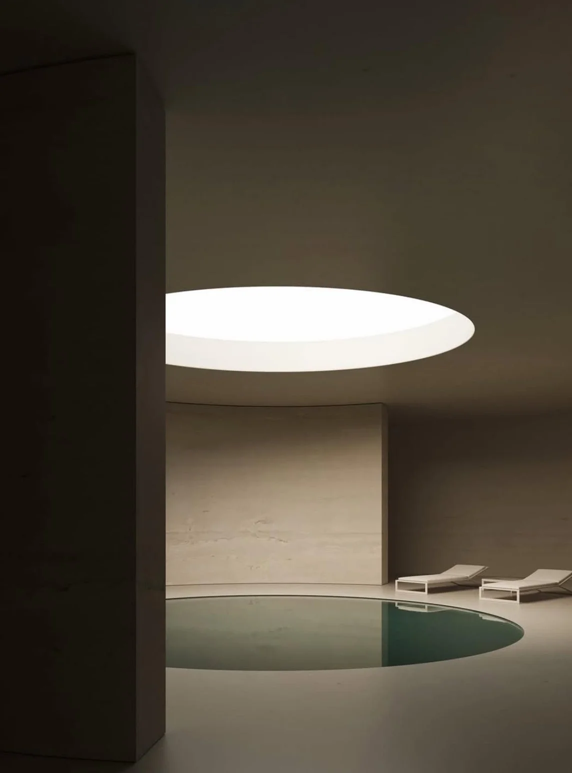 Minimalist indoor pool area with a round skylight ceiling, two lounge chairs beside the pool, and smooth, curved walls.
