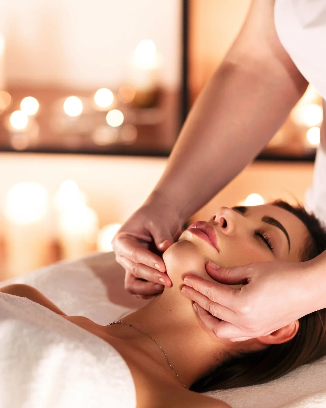 Person receiving facial massage at spa with candlelit background