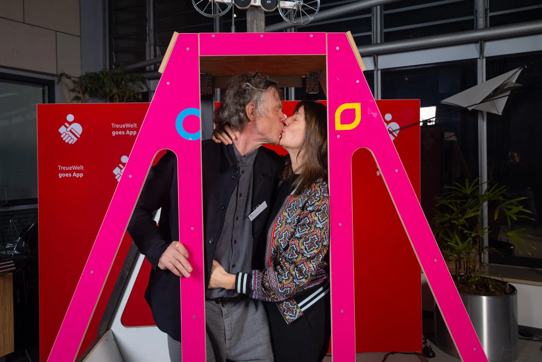 Zwei Menschen küssen sich in einer Fotokabine mit pinkem Rahmen bei einer Veranstaltung.