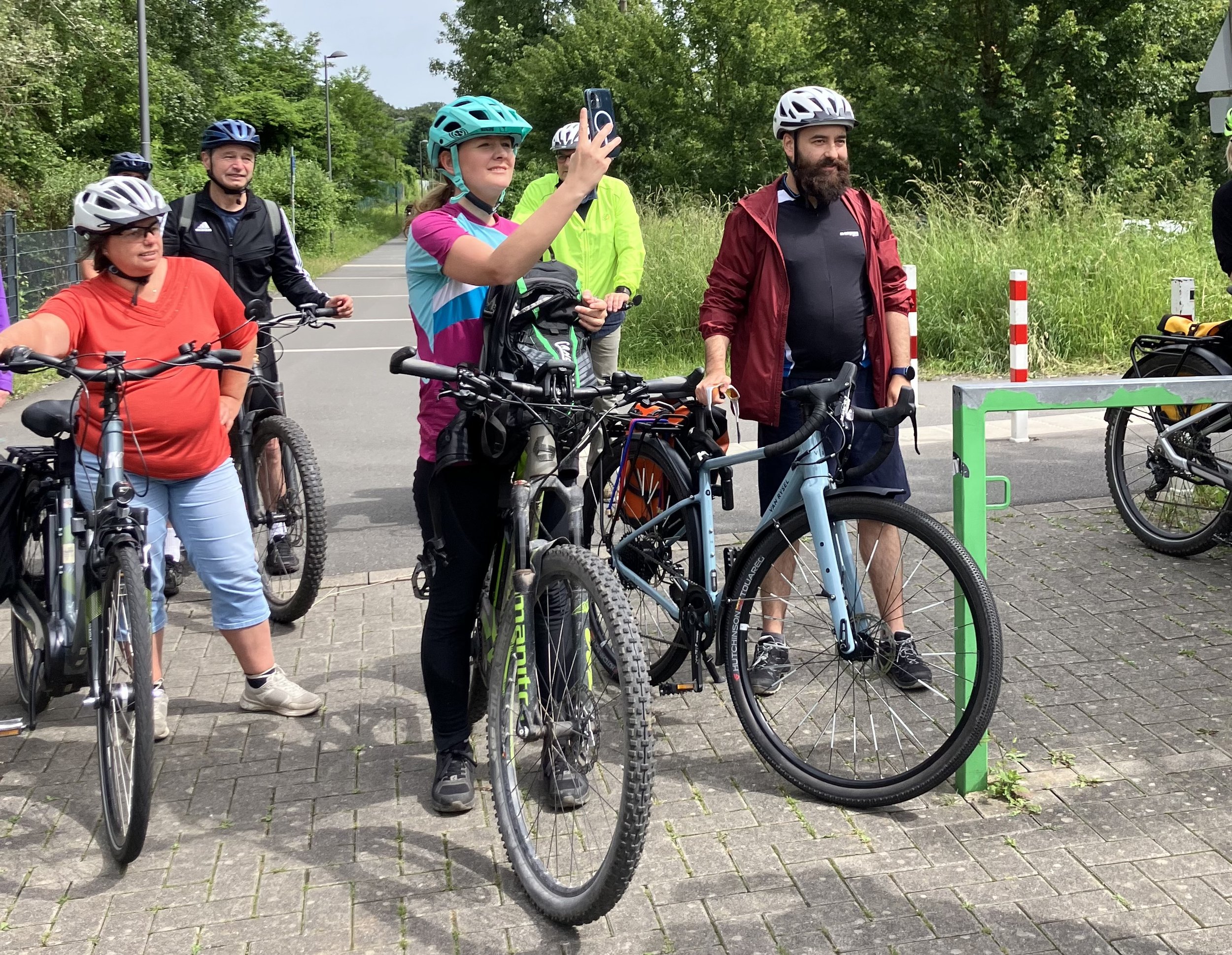 Das Bild zeigt eine Gruppe Menschen mit Fahrrädern. Sie machen Pause. Wuppertals Oberbürgermeisterin Miriam Scherff ist eine der Radfahrenden und macht ein Selfie.